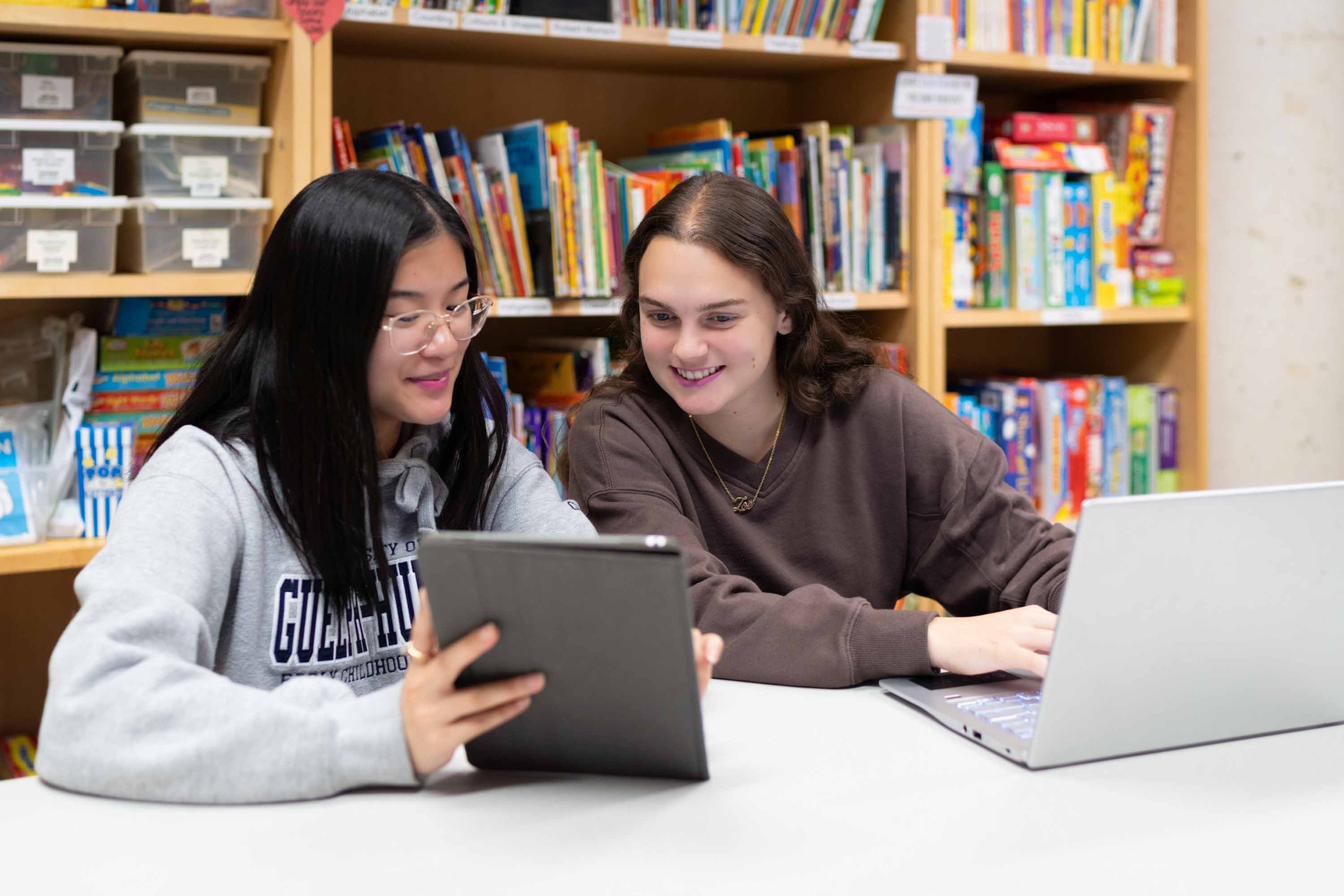 Students in a colourful room sitting at a desk, looking at laptops and tablets