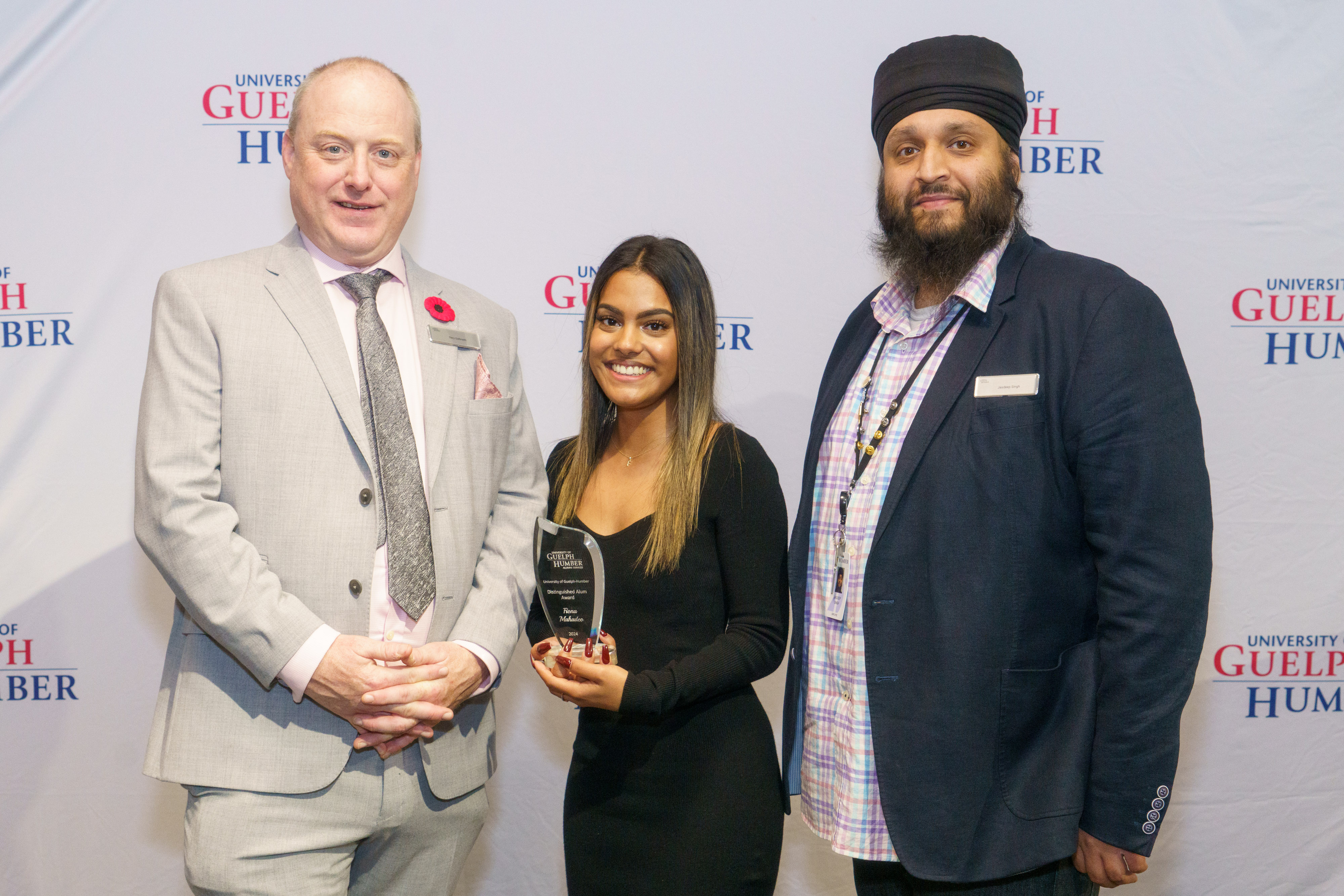 Two men and a woman pose for a photo as the woman holds a glass award