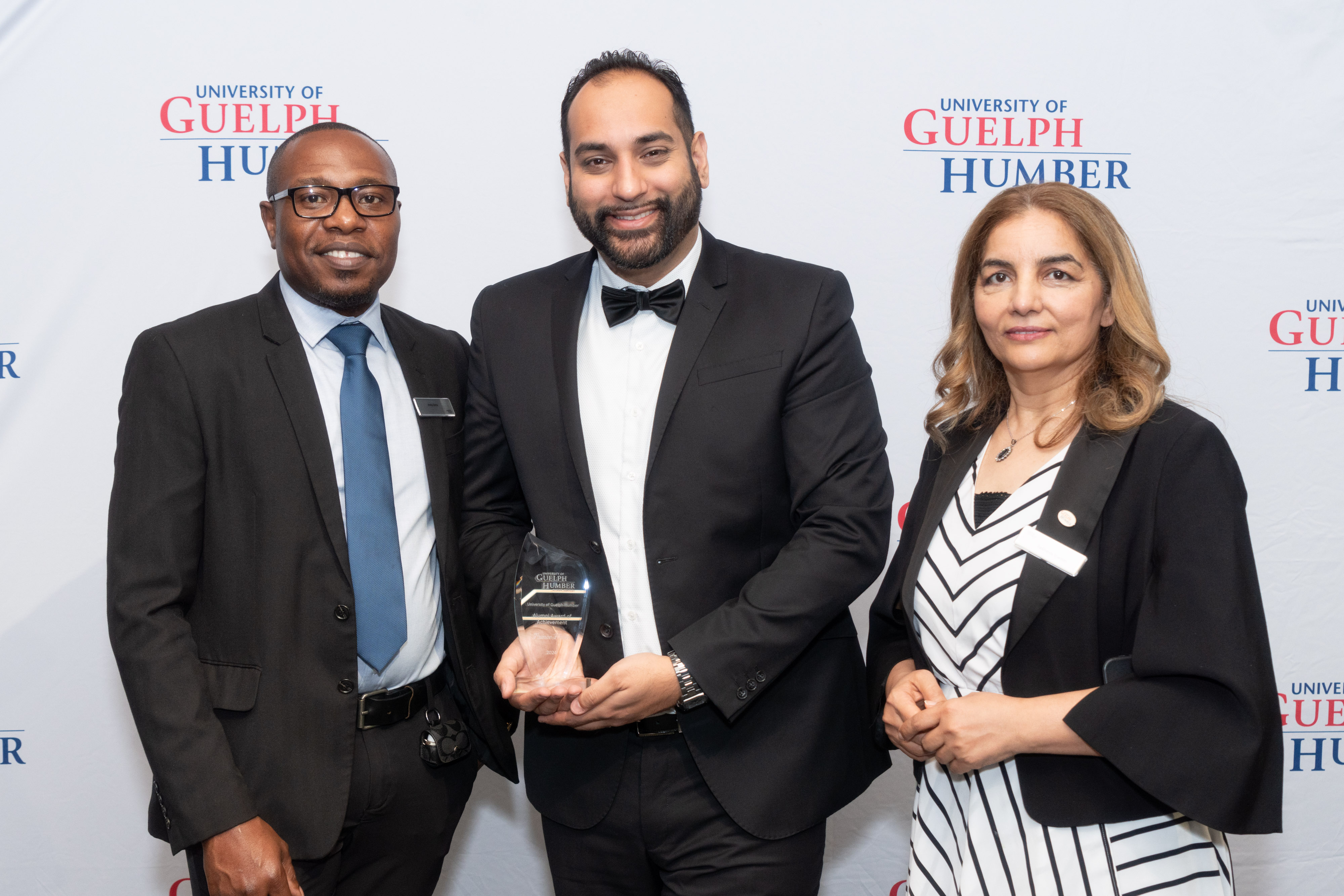 Two men and a woman pose for a photo as a man holds a glass award