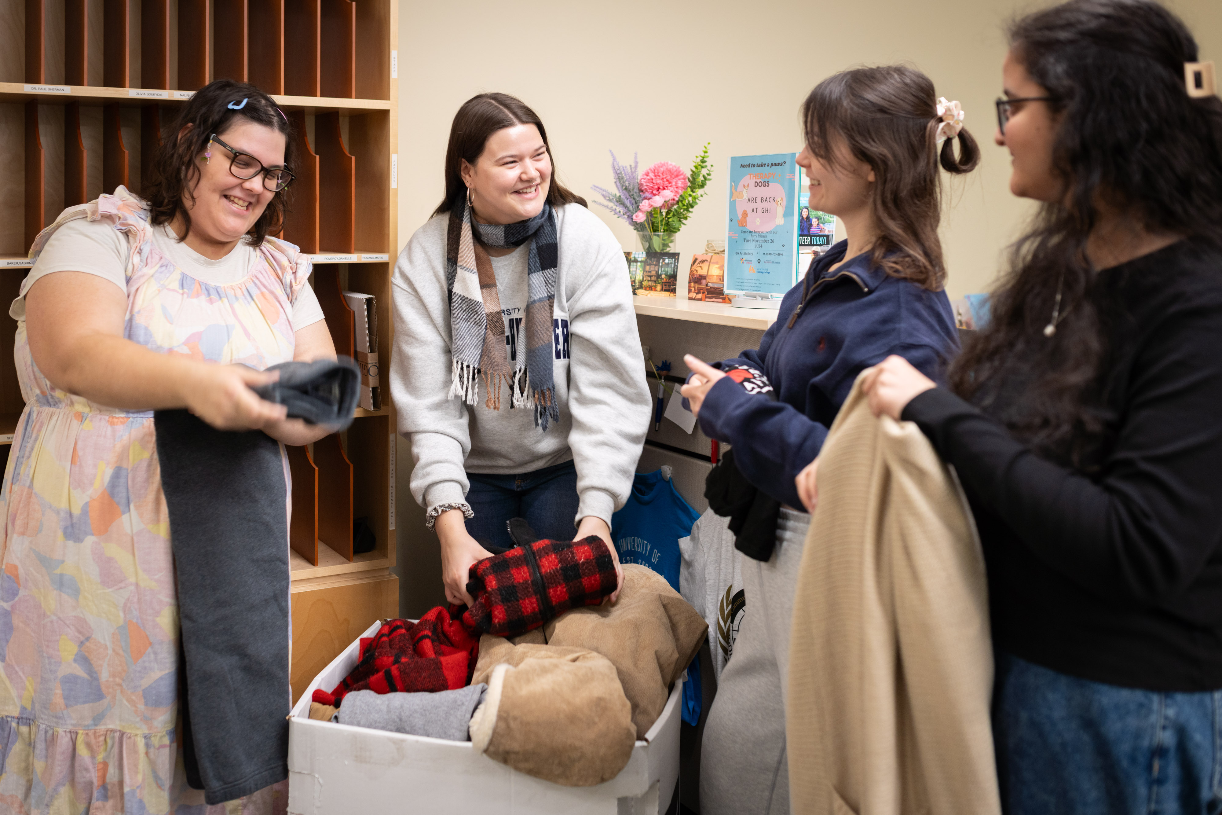 A group of four students helps fold winter clothing donations by a collection bin