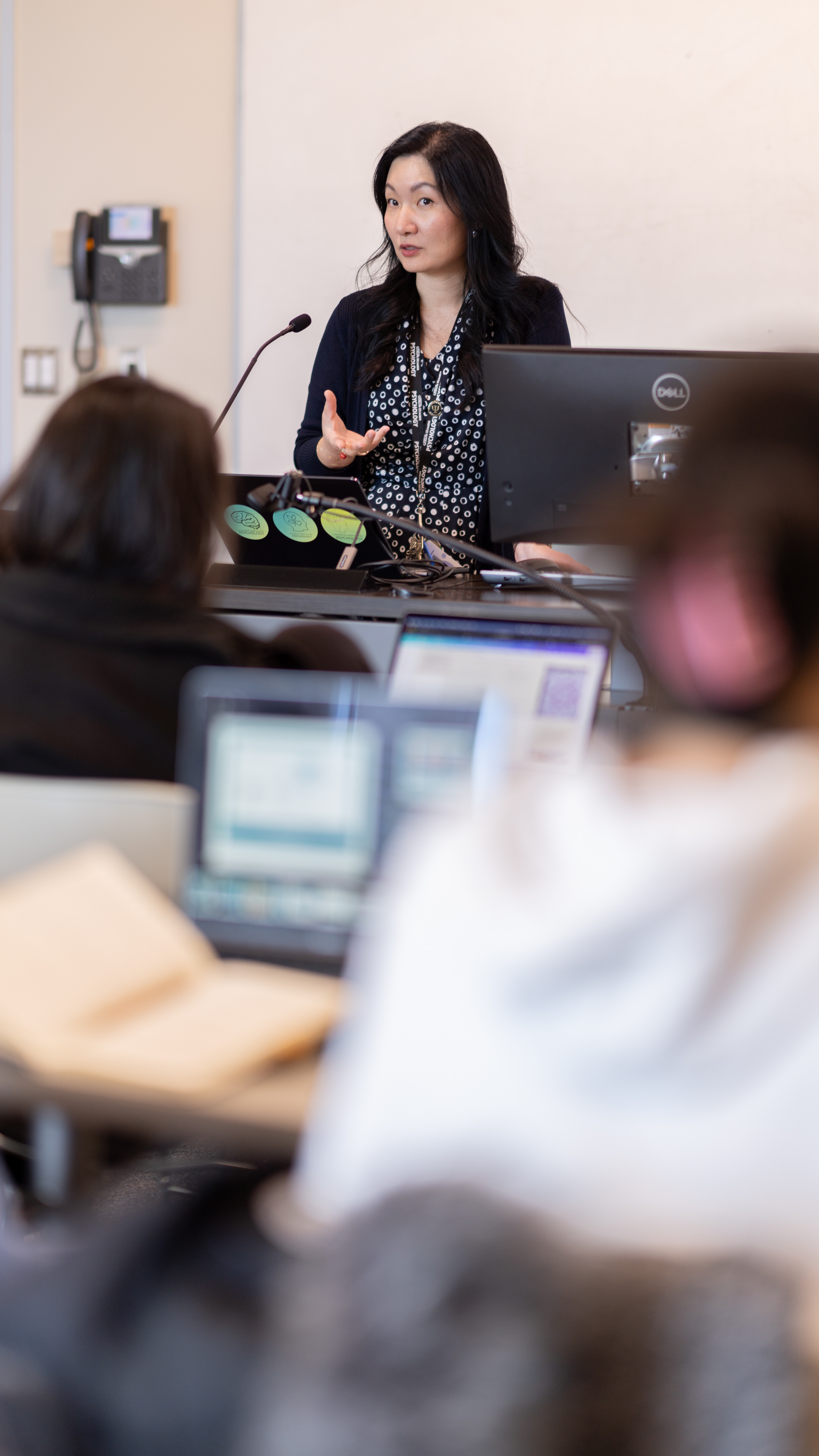 Alice Kim delivers a lecture behind a desk with a computer with a student audience in the foreground