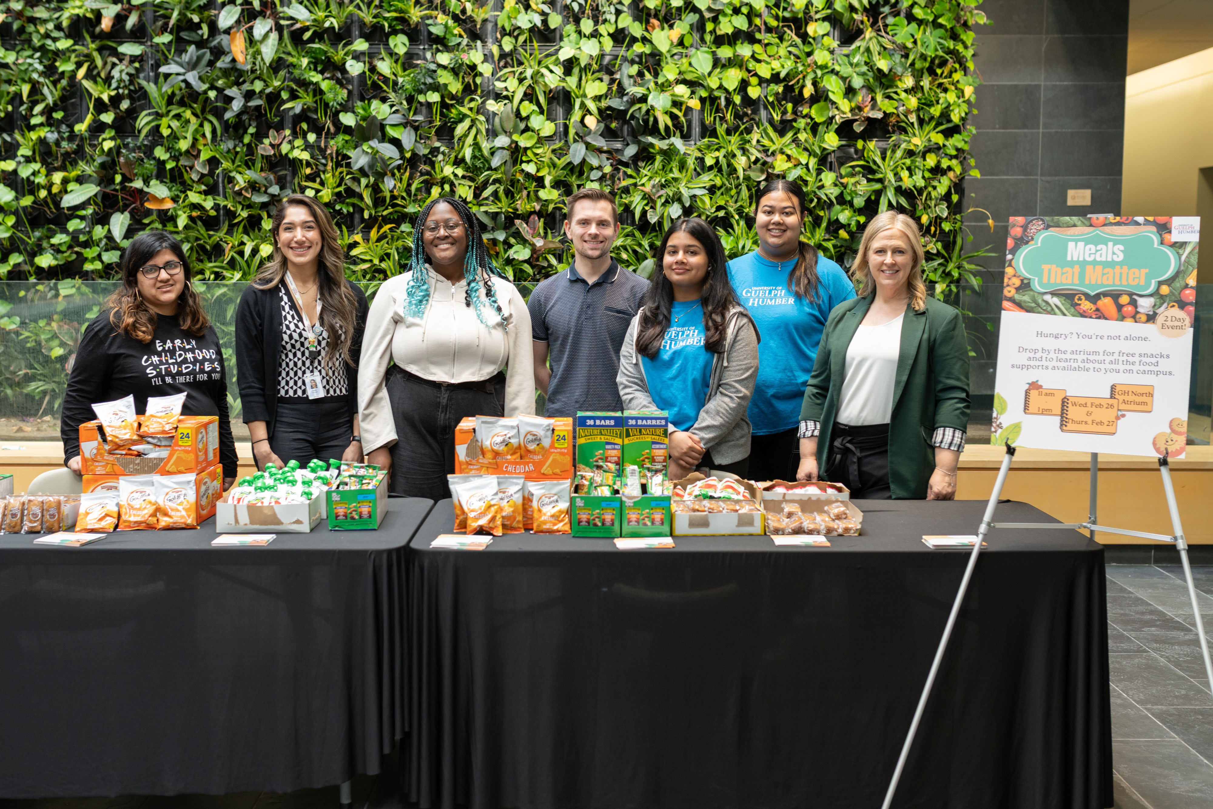 Seven people pose in front of the Meals That Matter table with snacks