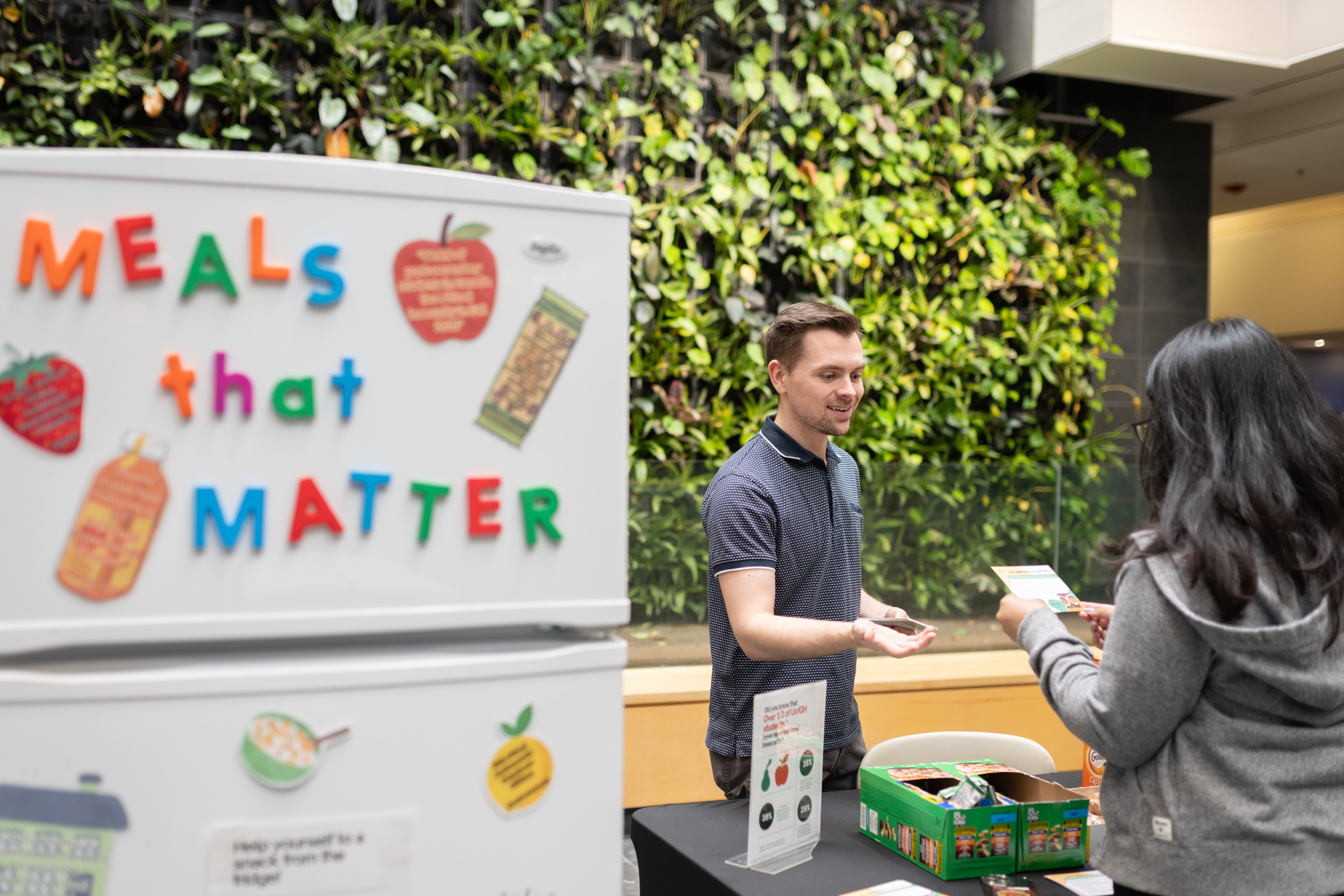 Staff helps students with snacks at Meals That Matter event beside fridge