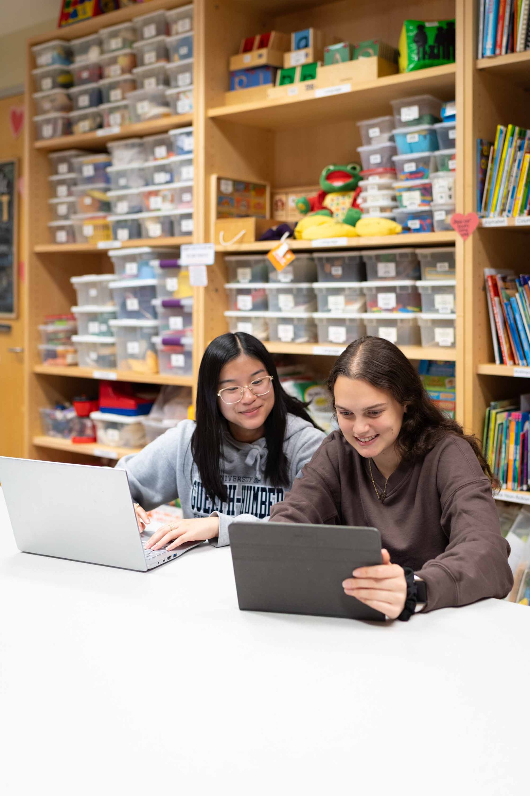 Students in a colourful room sitting at a desk, looking at laptops and tablets