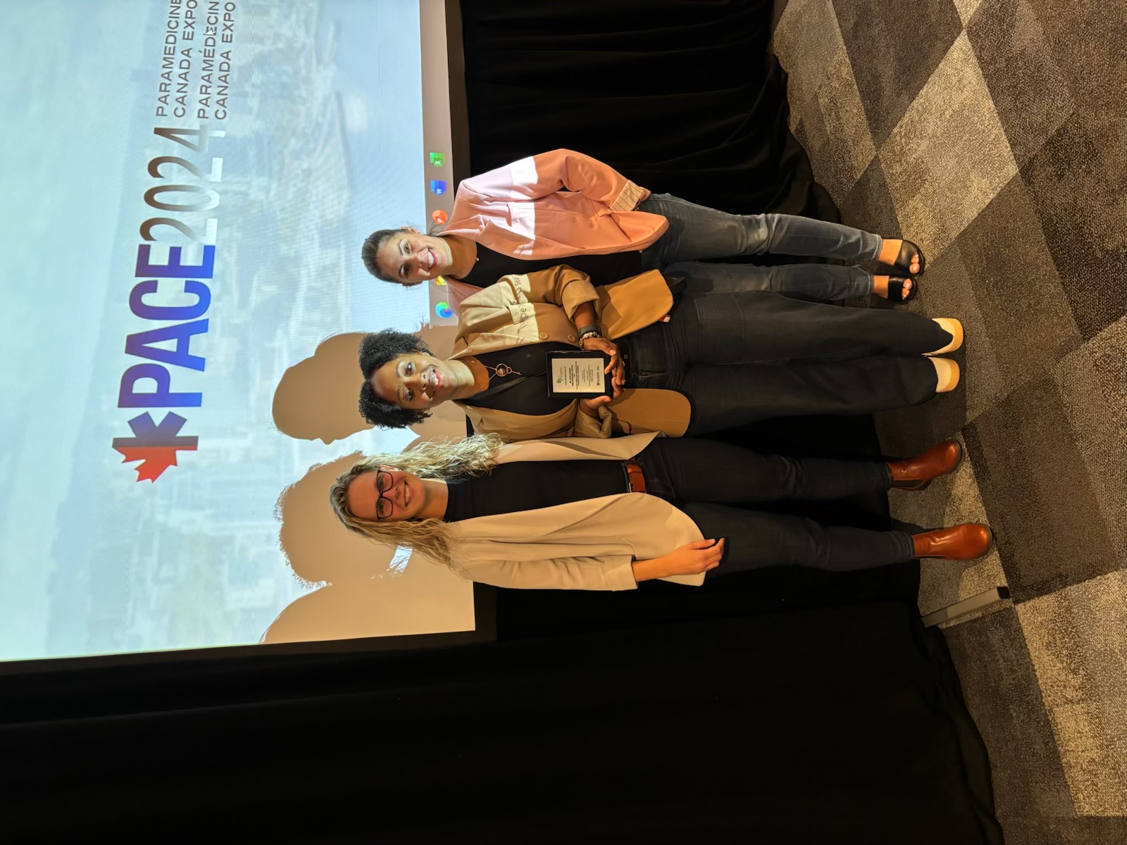 Three people holding award plaque in front of a screen