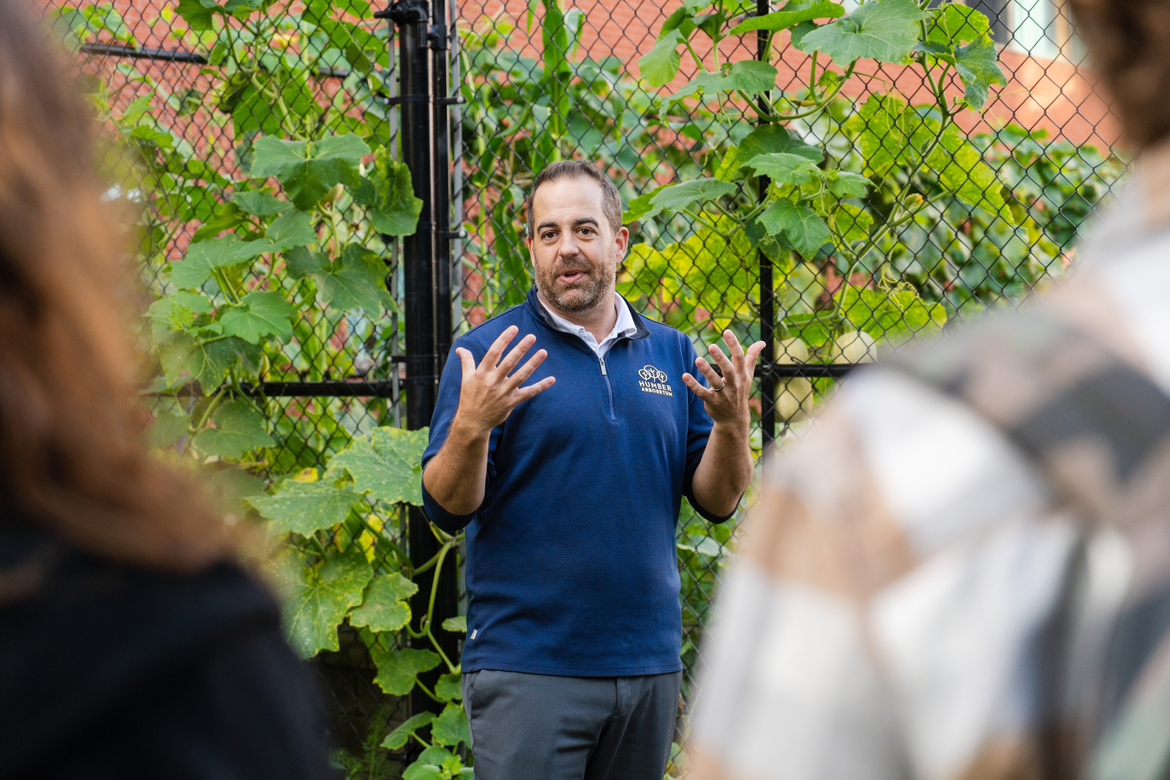 A man speaking in front of a green garden