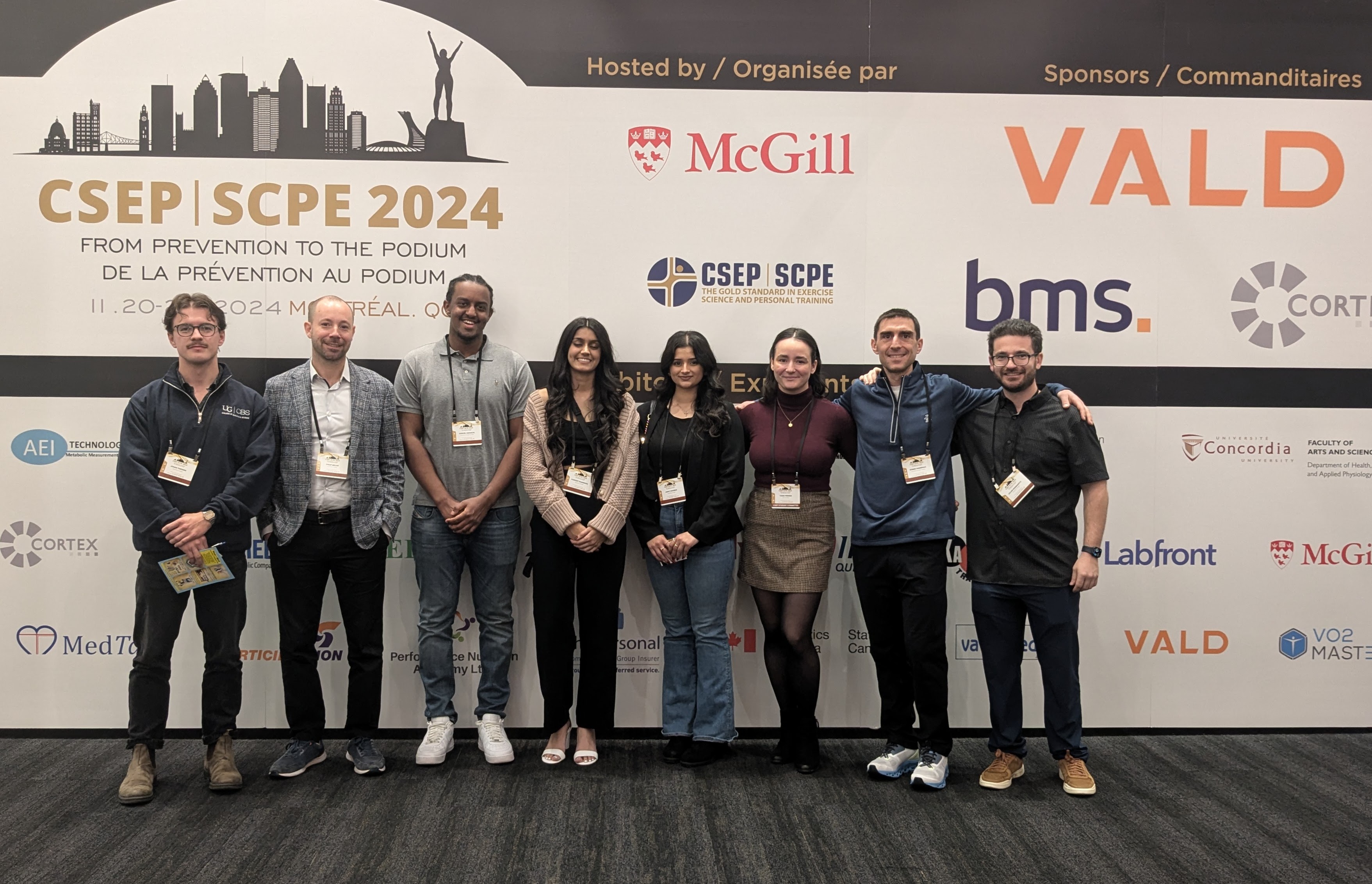 A group of eight people pose for a photo against a wall with sponsor logos at CSEP