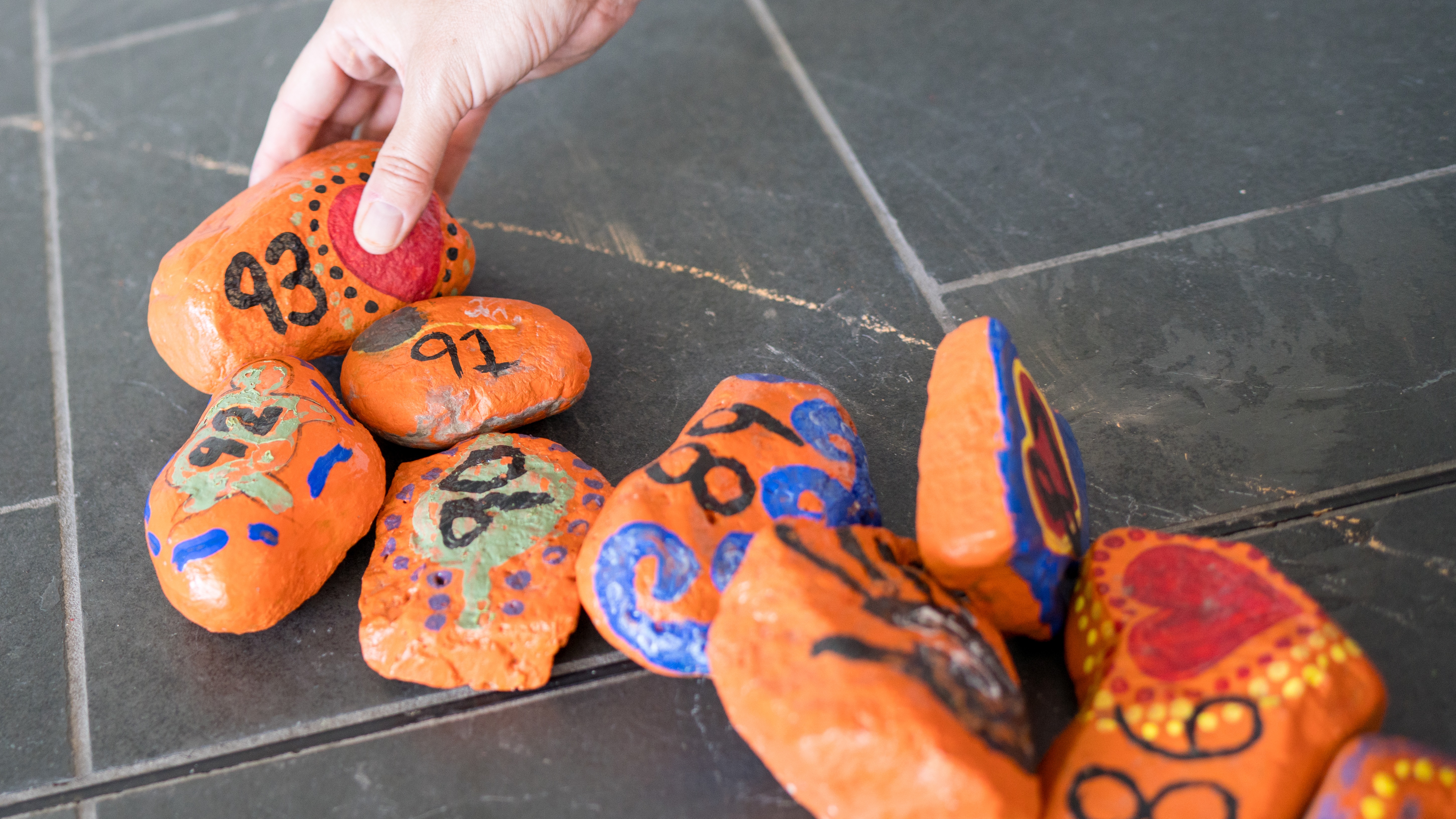 A hand placing rocks painted orange with numbers on them