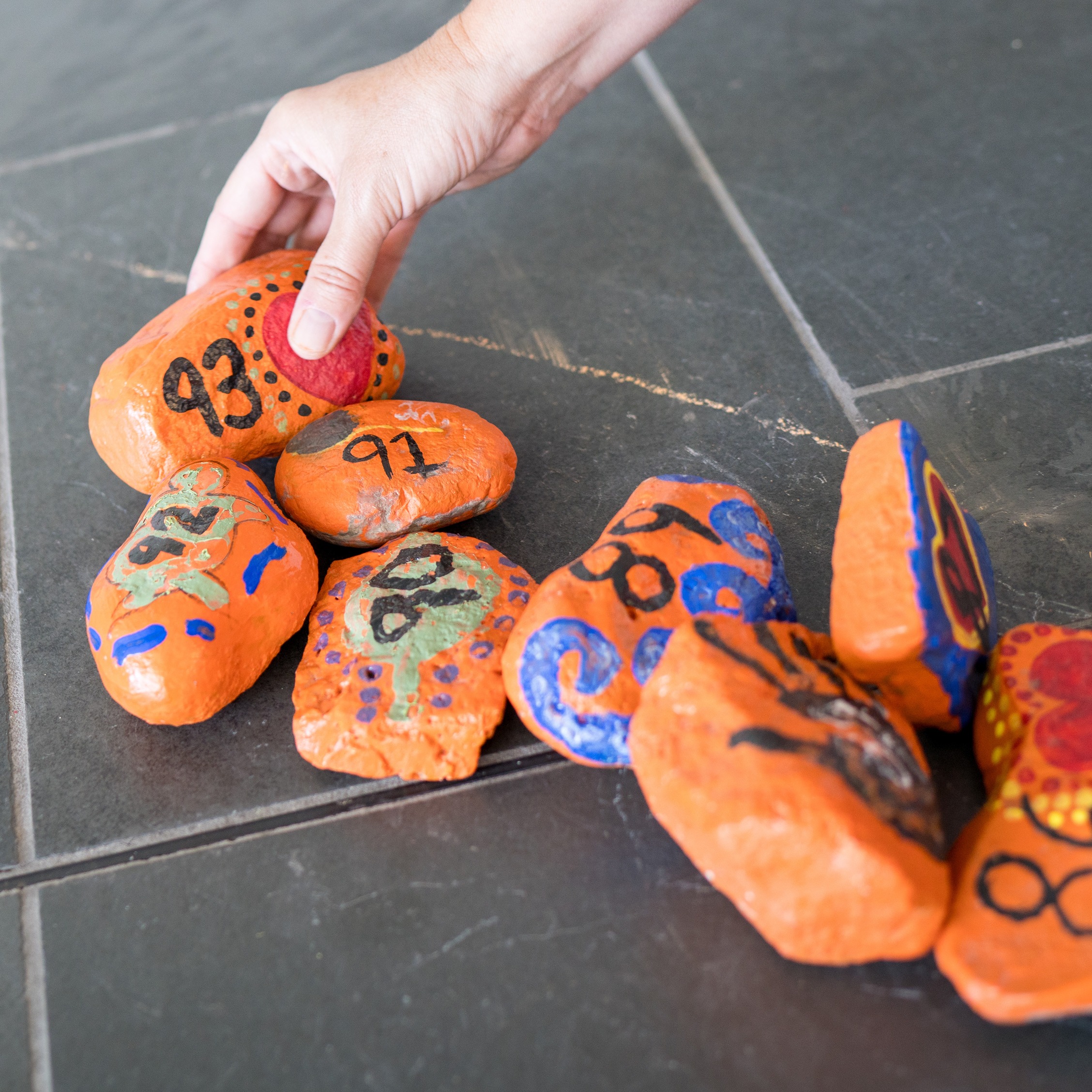 A hand placing rocks painted orange with numbers on them