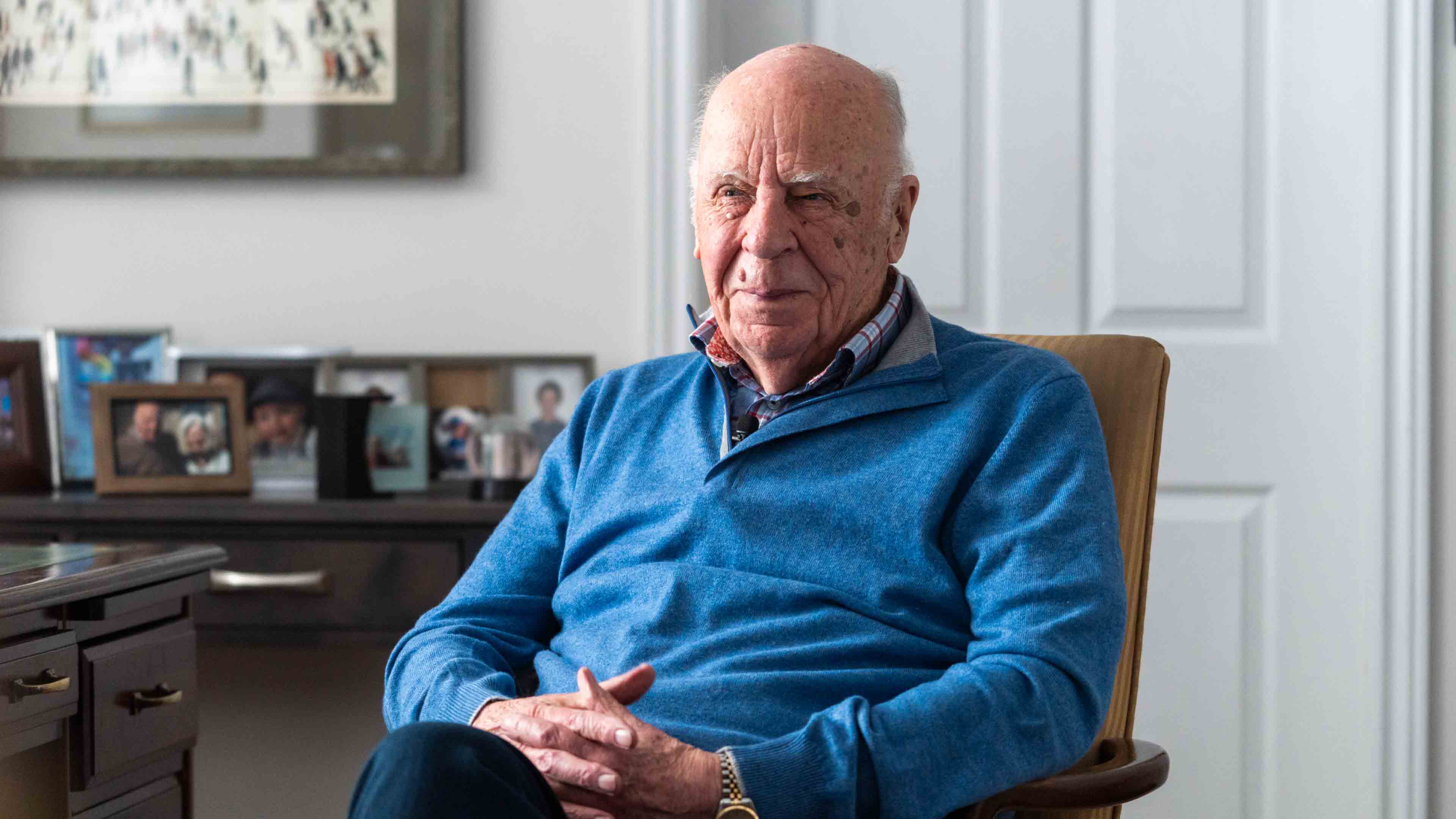 Dr. Michael Nightingale sits on a chair in his home, in the background there are pictures in frames