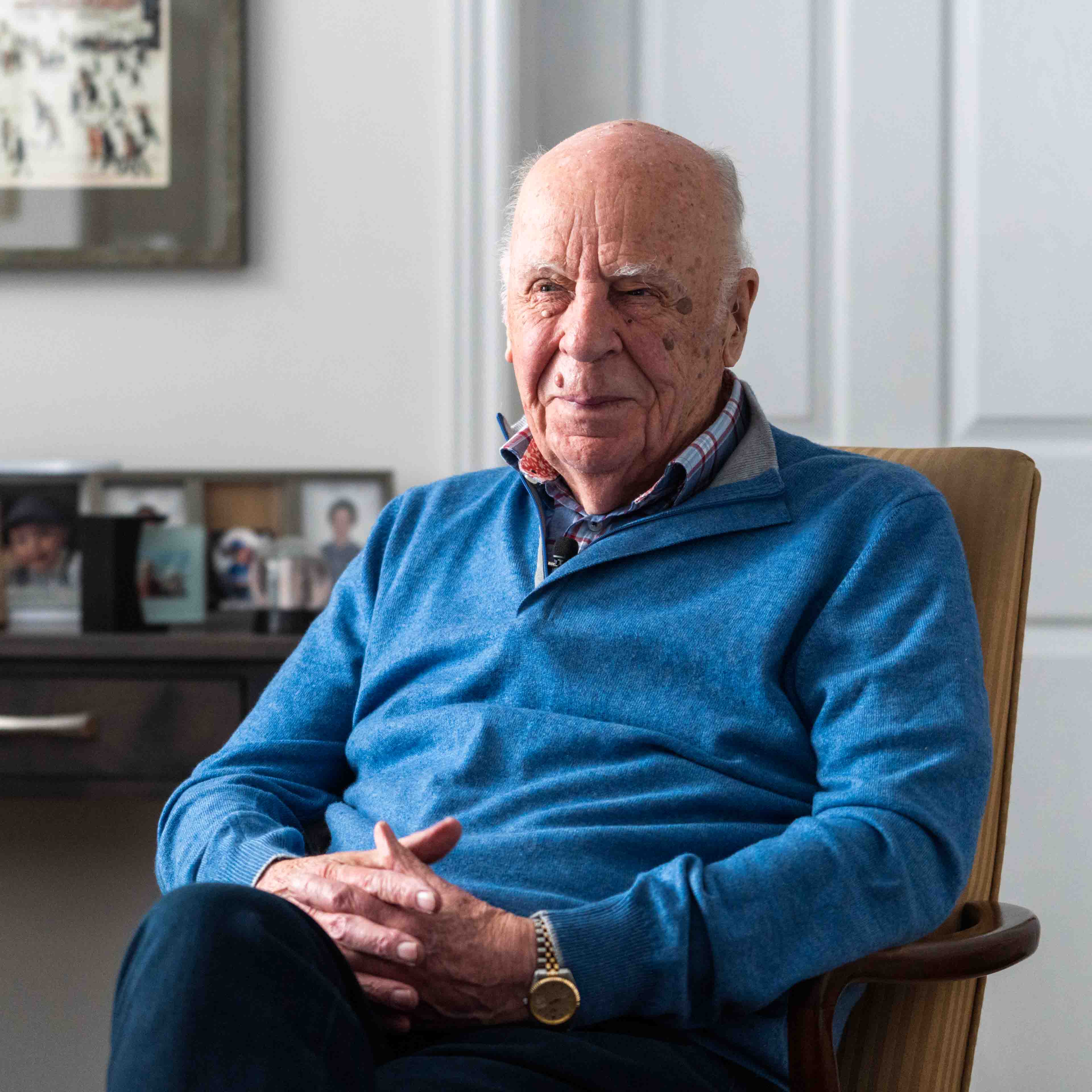 Dr. Michael Nightingale sits on a chair in his home, in the background there are pictures in frames