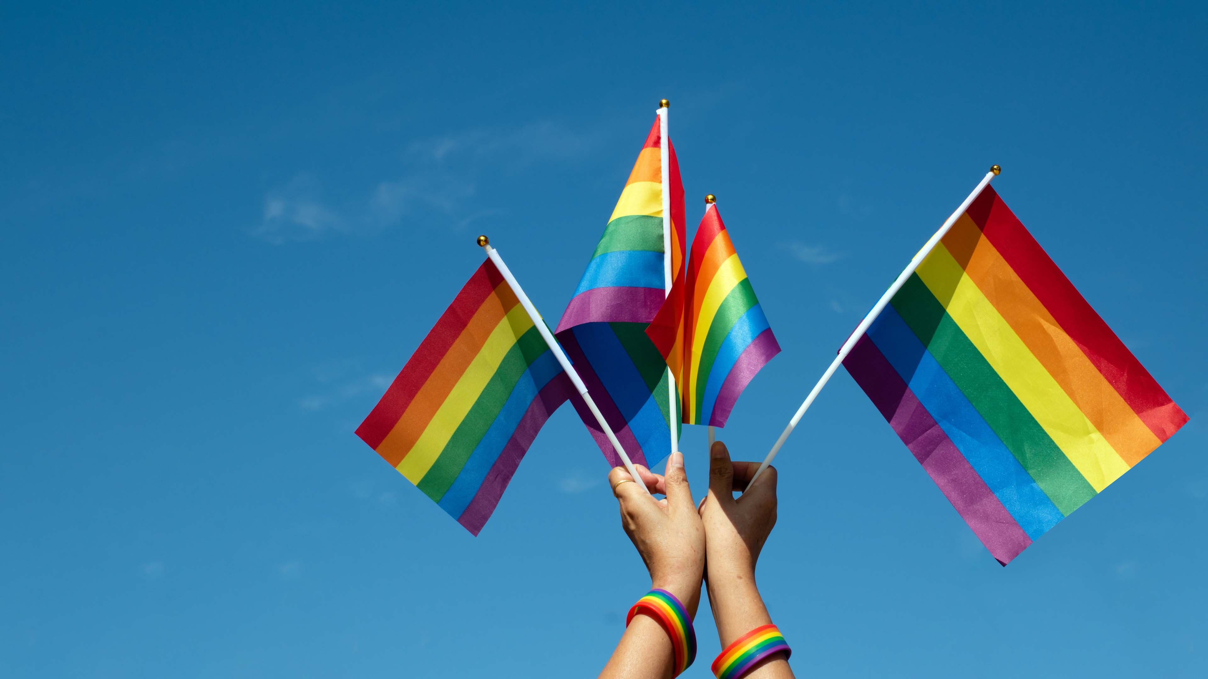 Two hands holding up four rainbow pride flags