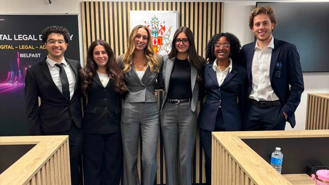 Six students stand at the front of a mock courtroom wearing suits