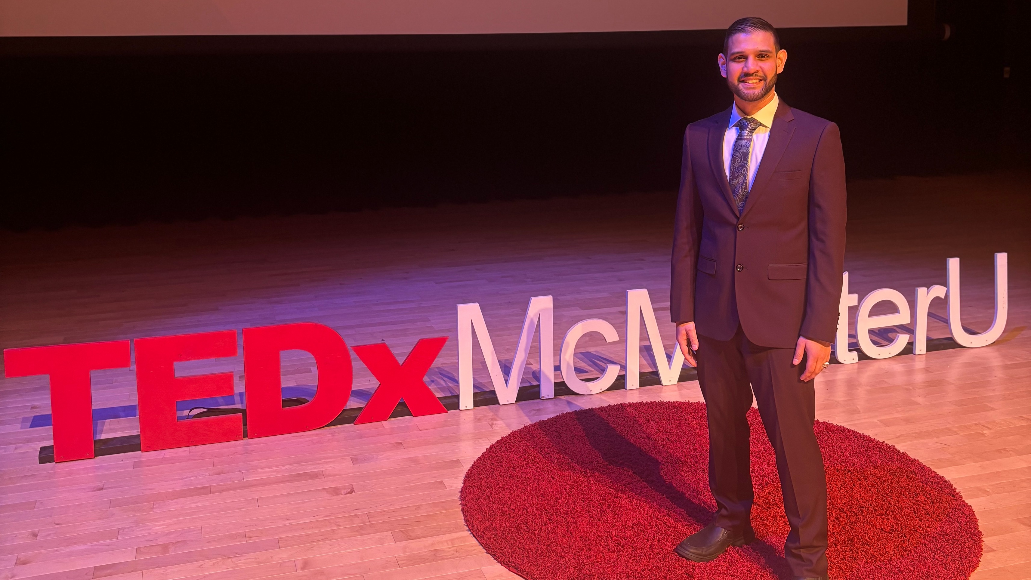 Basim Salim standing on a stage with letters that say TEDxMcMasterU