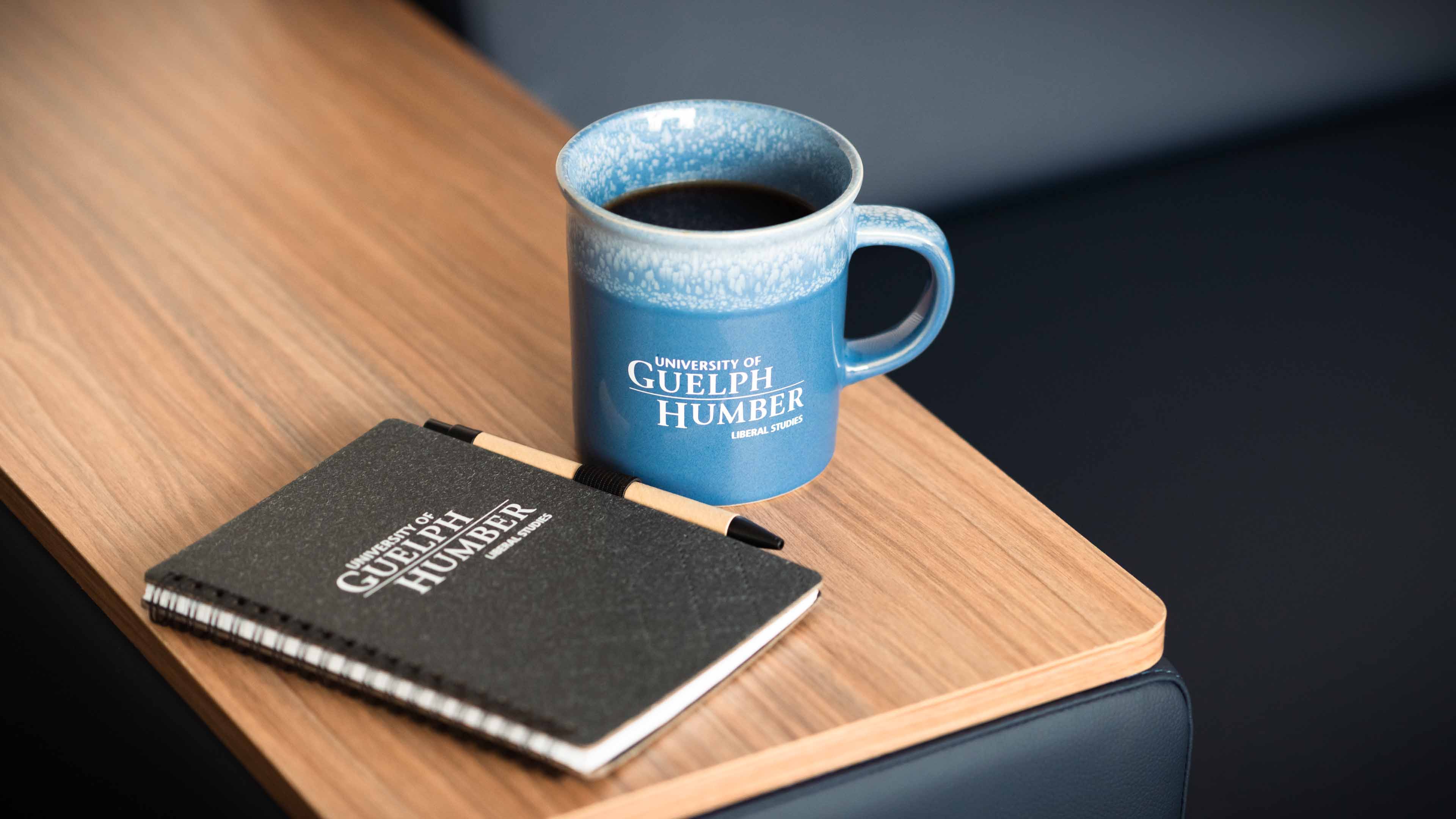 A notebook and coffee mug are on a table with the words "University of Guelph-Humber Liberal Studies"