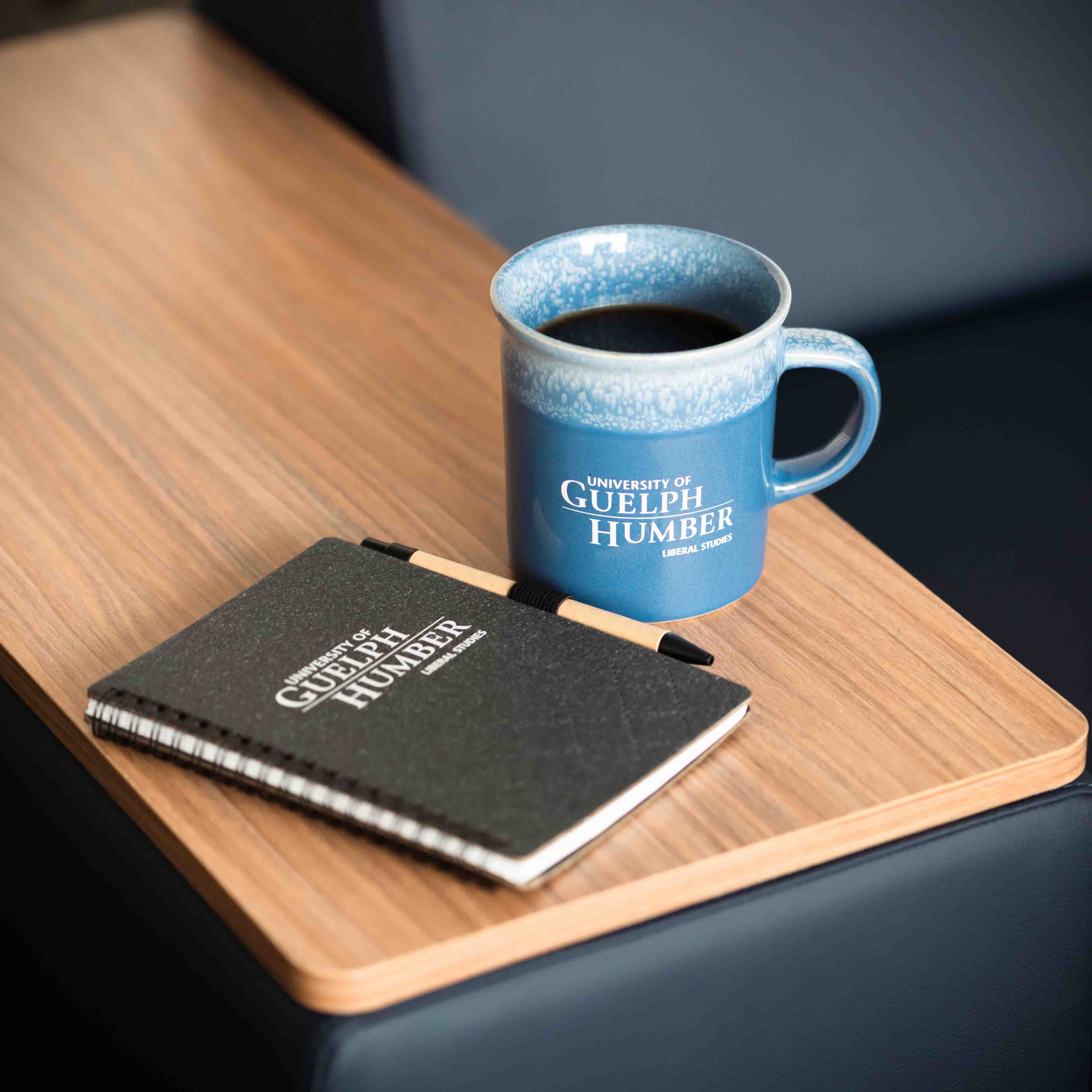 A notebook and coffee mug are on a table with the words "University of Guelph-Humber Liberal Studies"