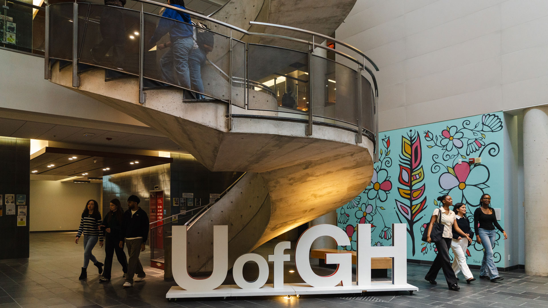 Interior shot of spiral staircase, students walking, and letter sign that says "U of GH"