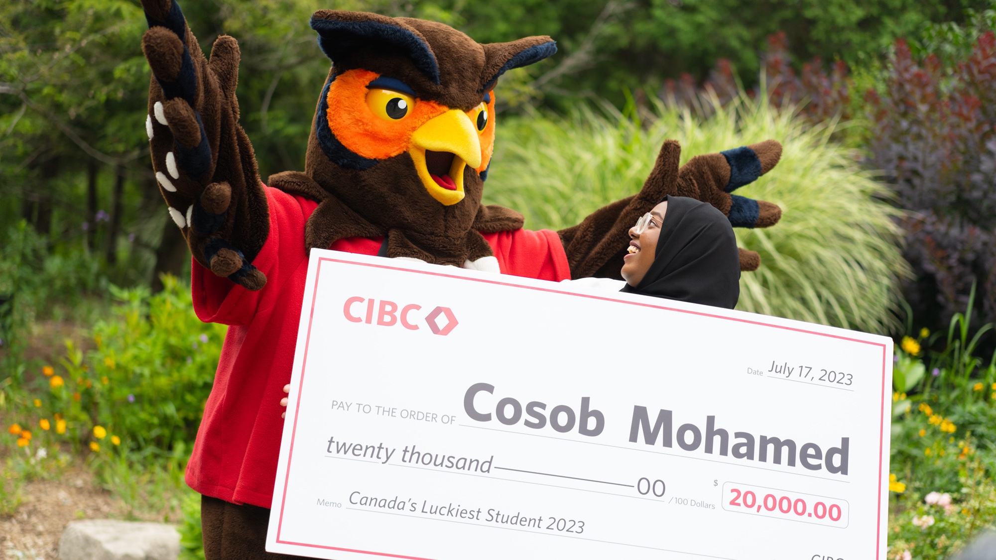 GH owl mascot with arms up as student holds giant cheque