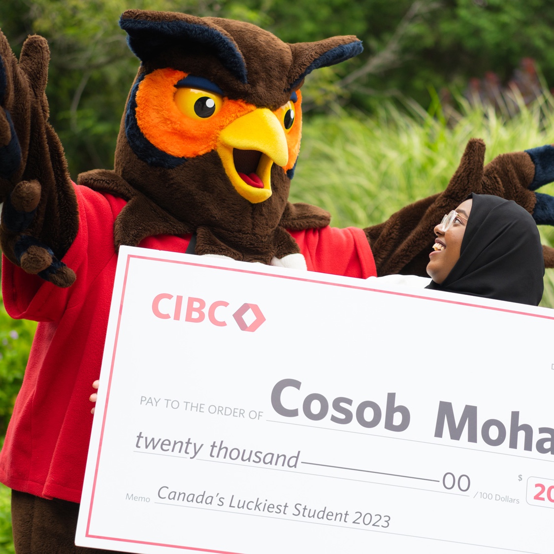 GH owl mascot with arms up as student holds giant cheque