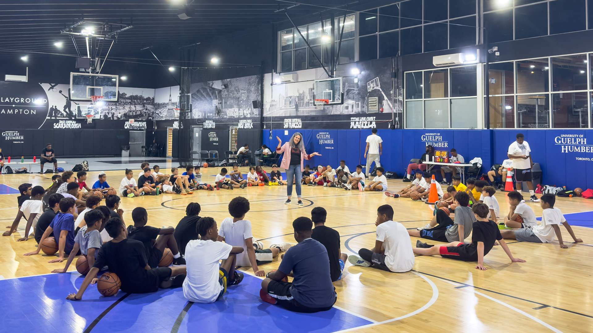 Group of young students sitting in a circle in a gym with Dr. Martyn speaking in middle