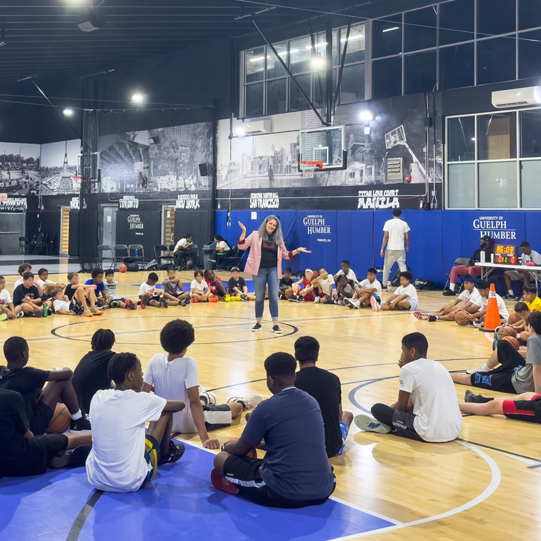 Group of young students sitting in a circle in a gym with Dr. Martyn speaking in middle