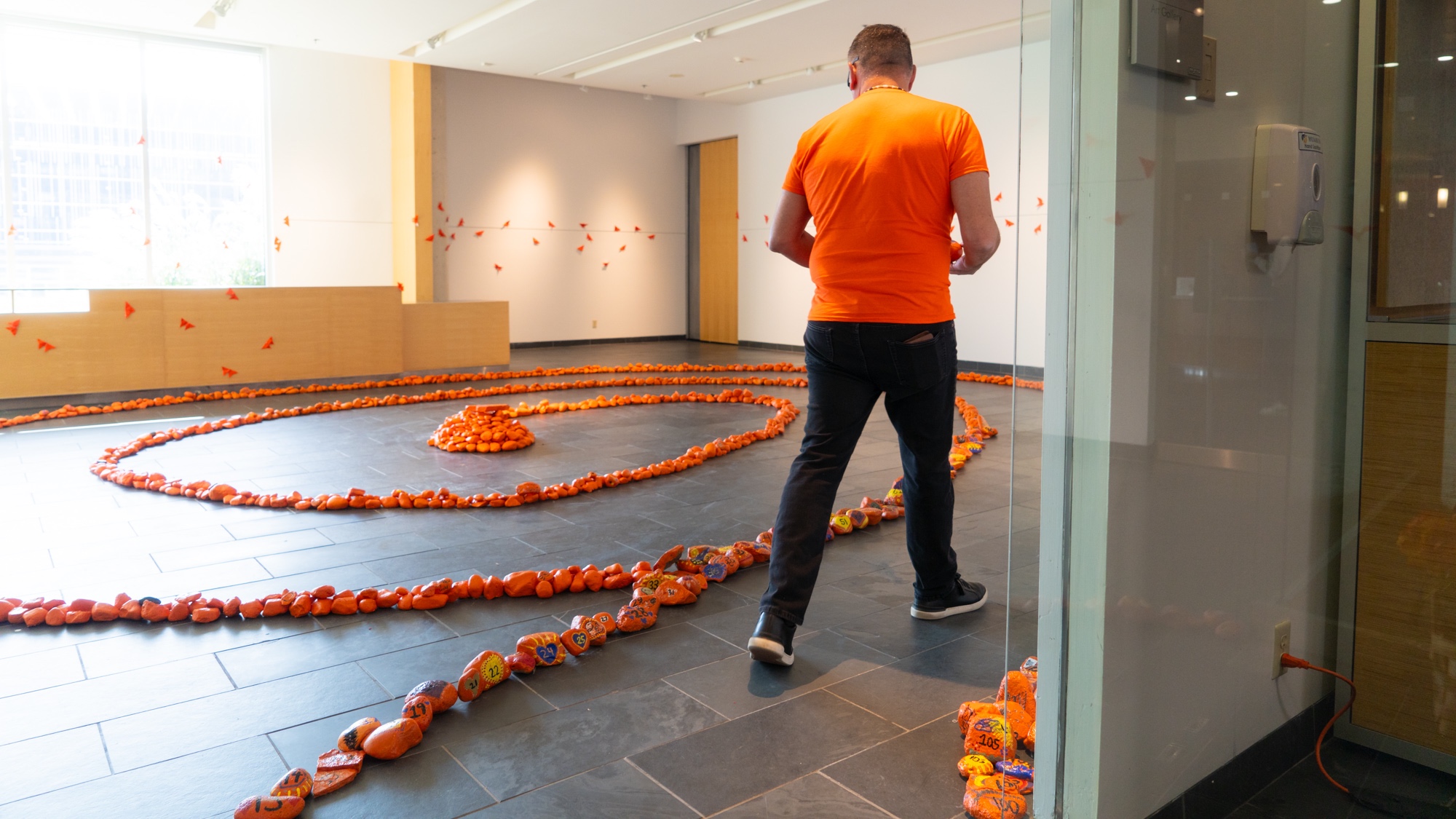 Man with orange shirt looking at display of orange rocks on gallery floor