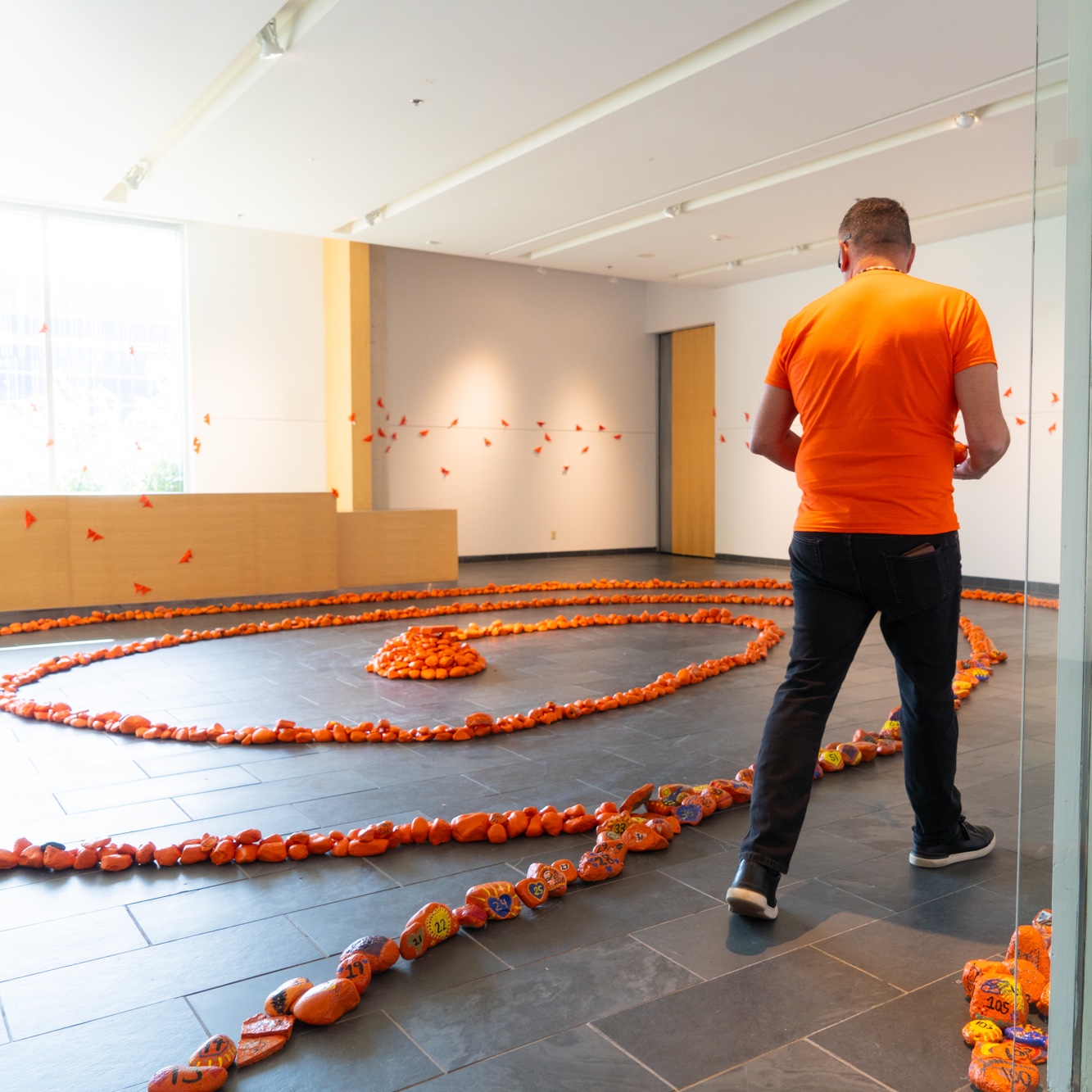 Man with orange shirt looking at display of orange rocks on gallery floor