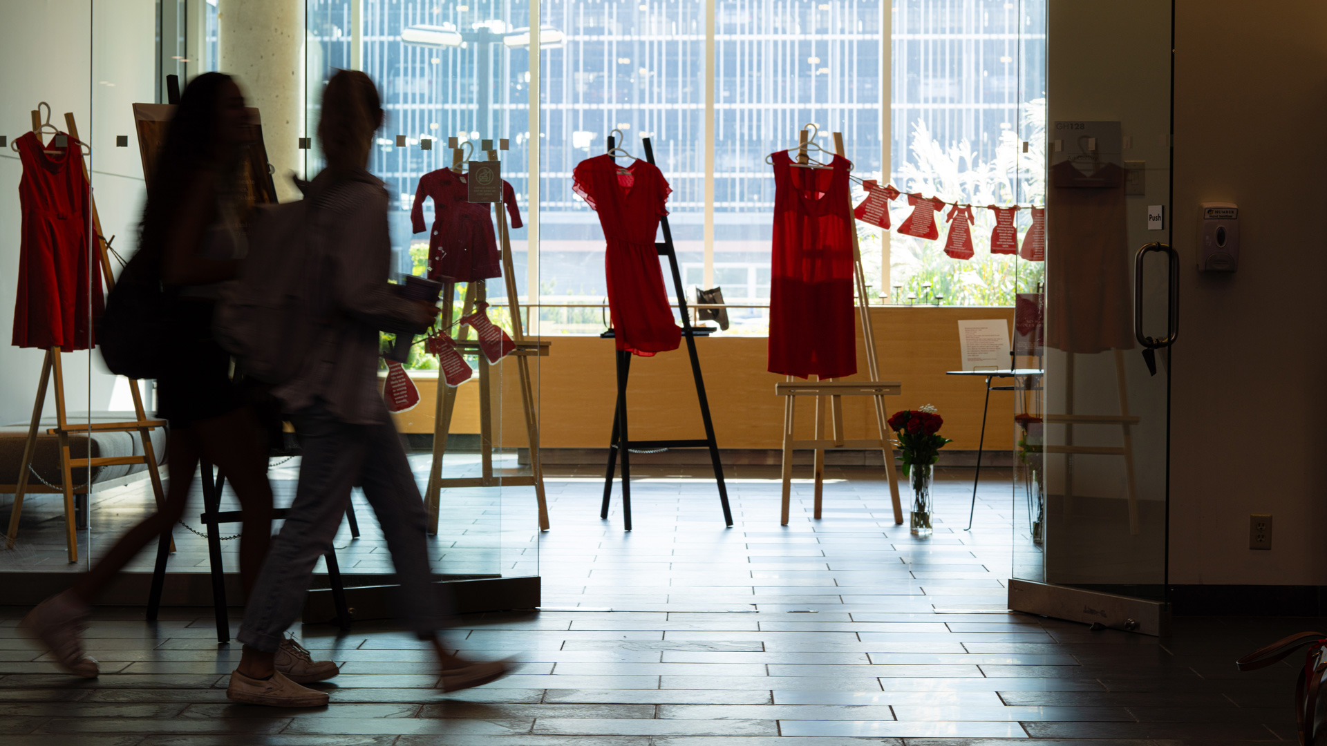 Two students walking by a display of red dresses on easels