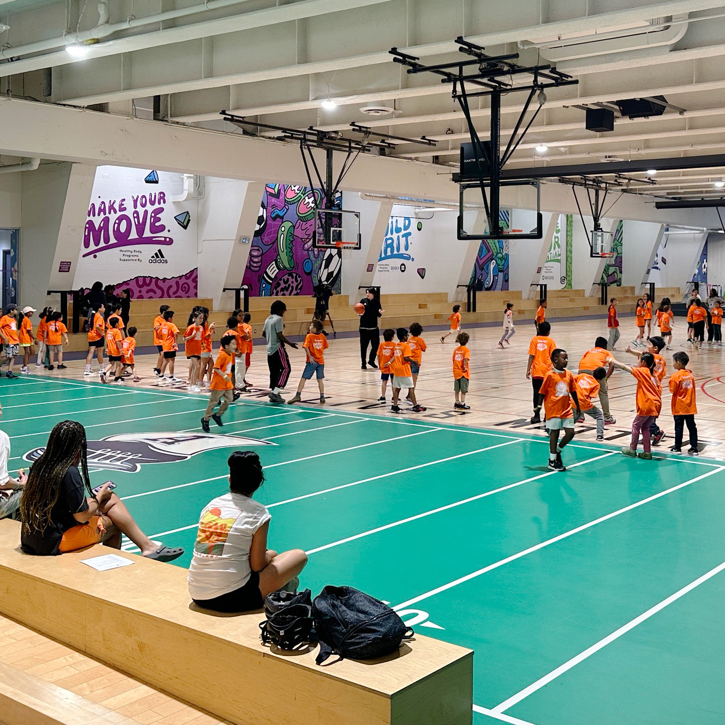 A group of children wearing orange t-shirts in a gym running around