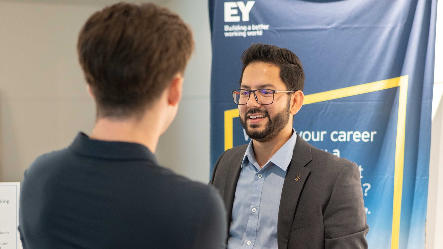 A man in a suit speaks to a UofGH student at a networking event