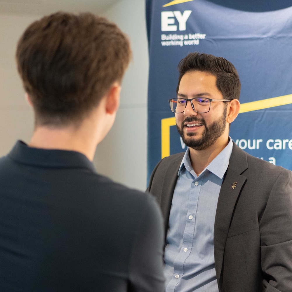 A man in a suit speaks to a UofGH student at a networking event