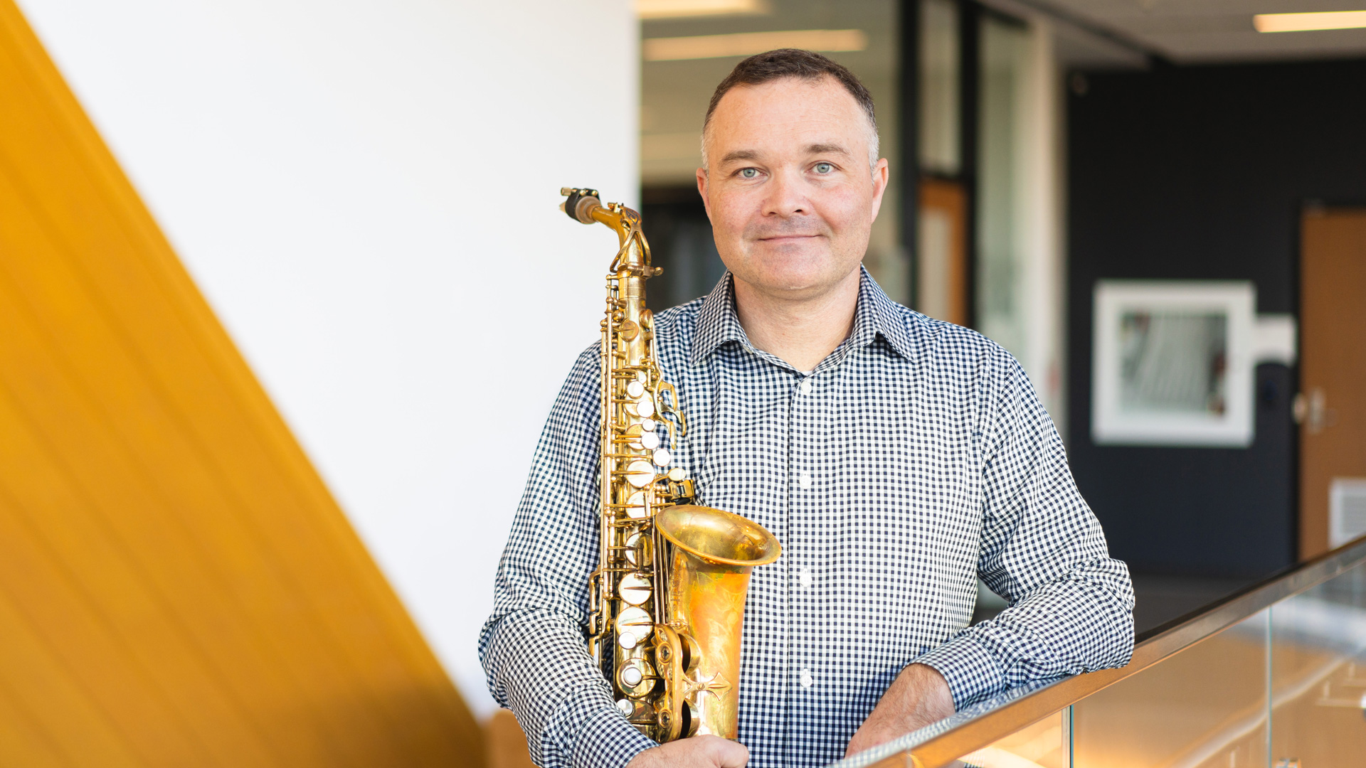 Dr. Ryan Bruce holding a saxophone in his right arm while looking at the camera