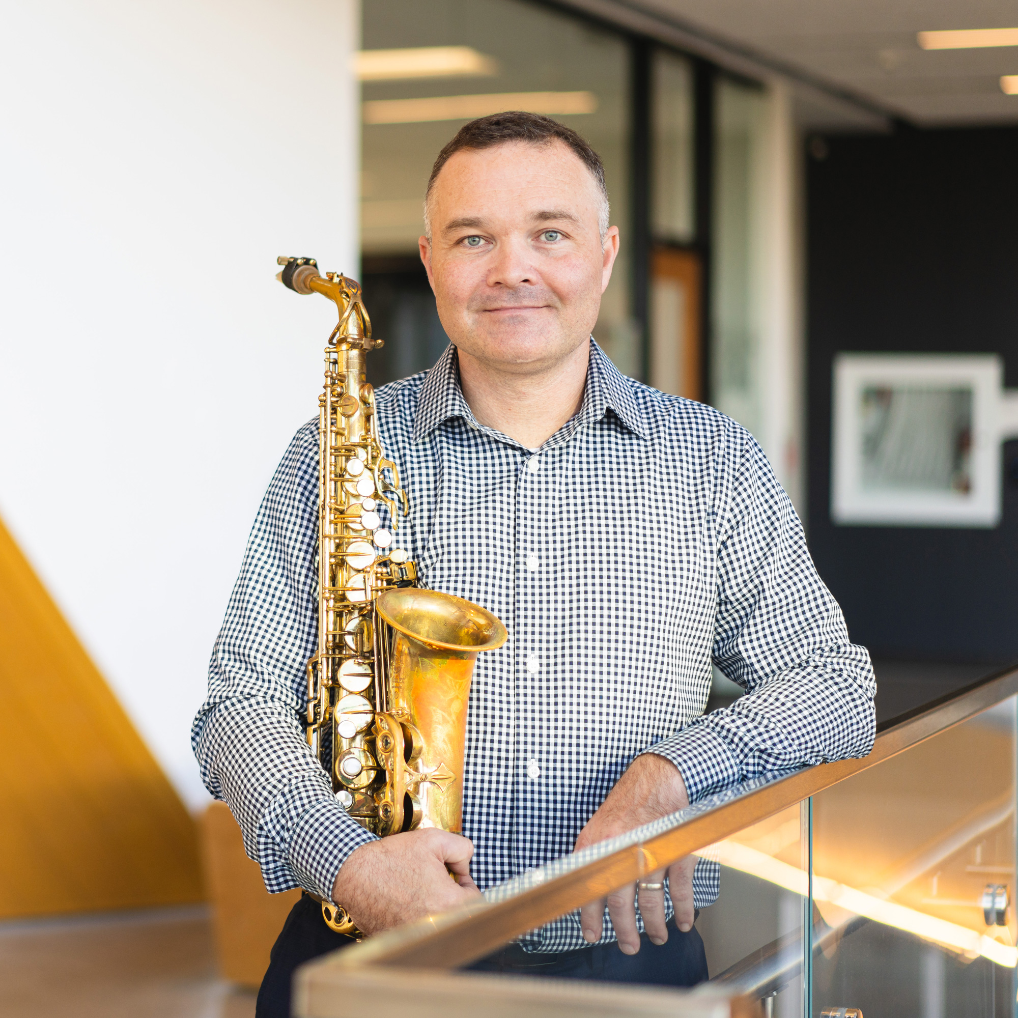 Dr. Ryan Bruce holding a saxophone in his right arm while looking at the camera