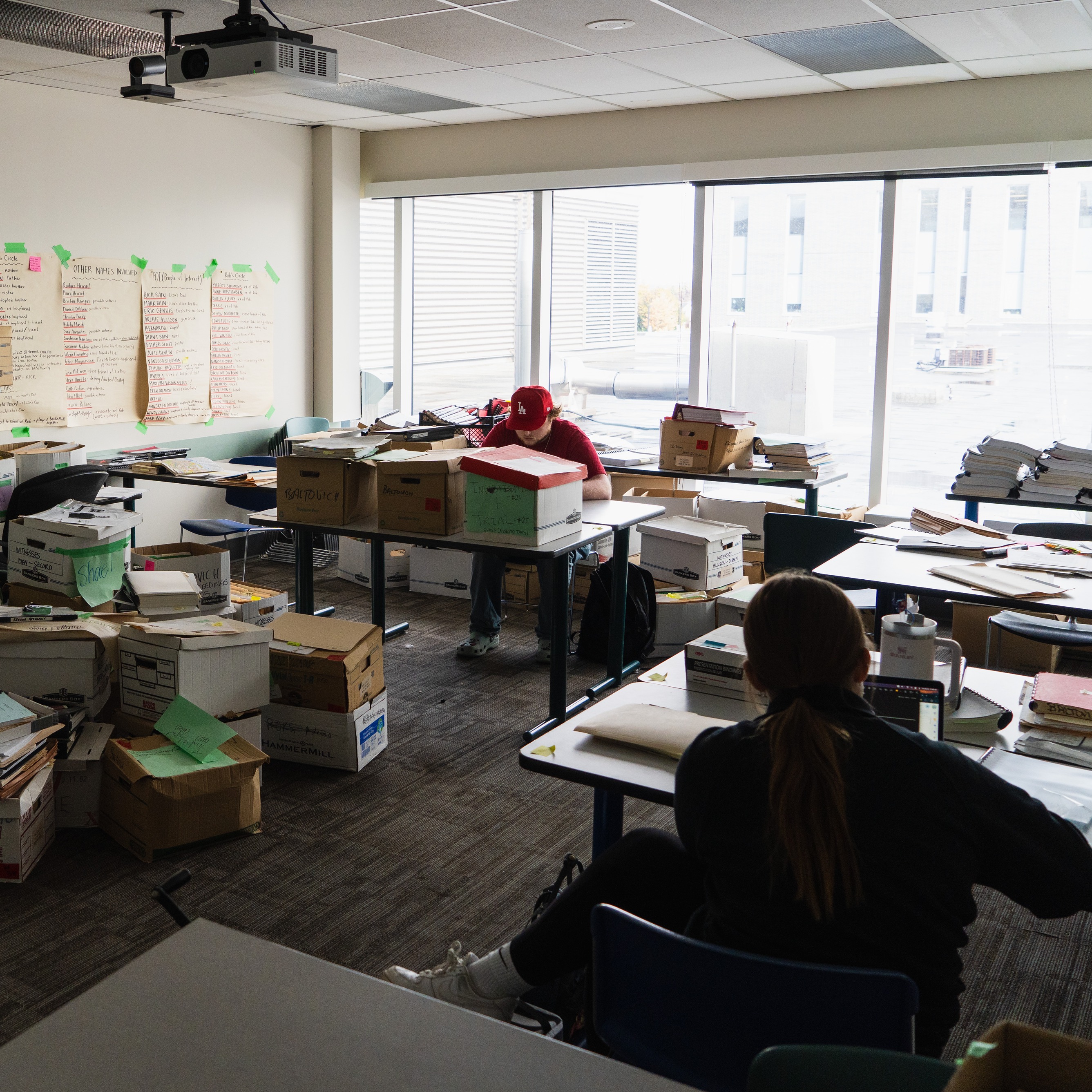 Room filled with boxes and files, with two students reviewing documents