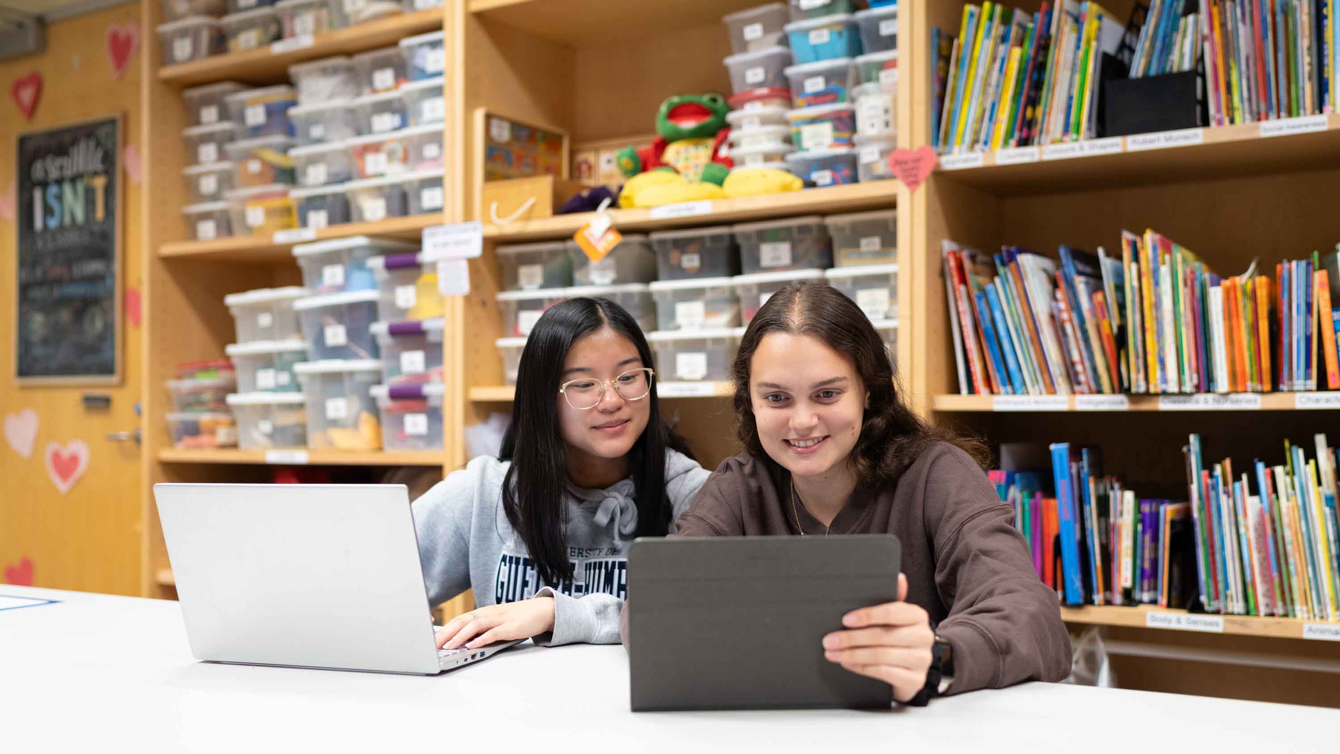 Students in a colourful room sitting at a desk, looking at laptops and tablets