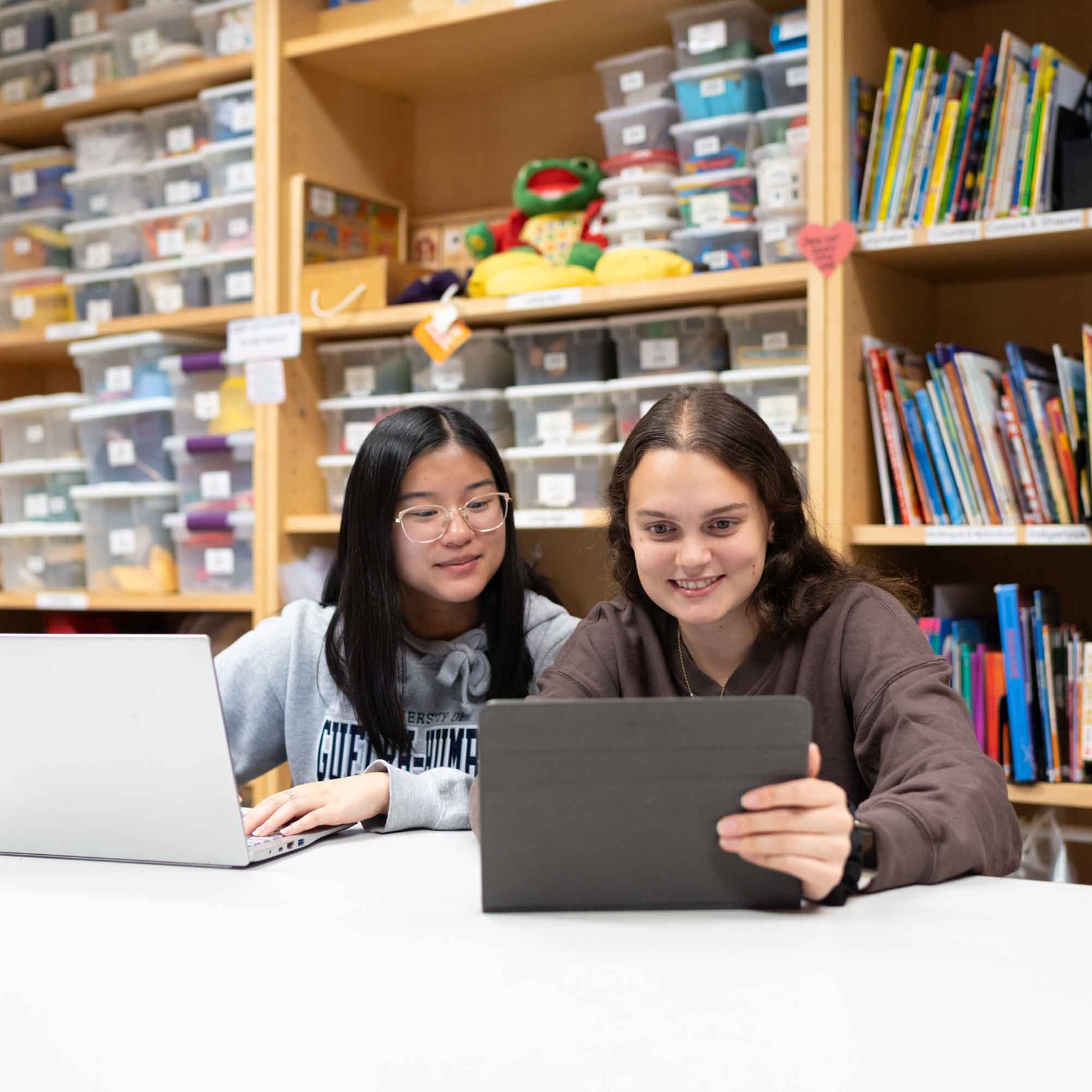 Students in a colourful room sitting at a desk, looking at laptops and tablets