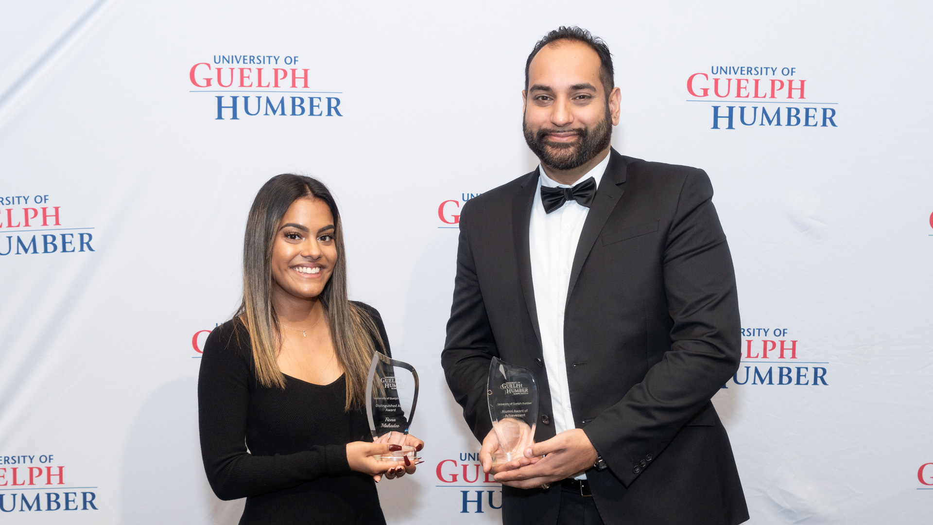 A woman and a man each hold a glass award