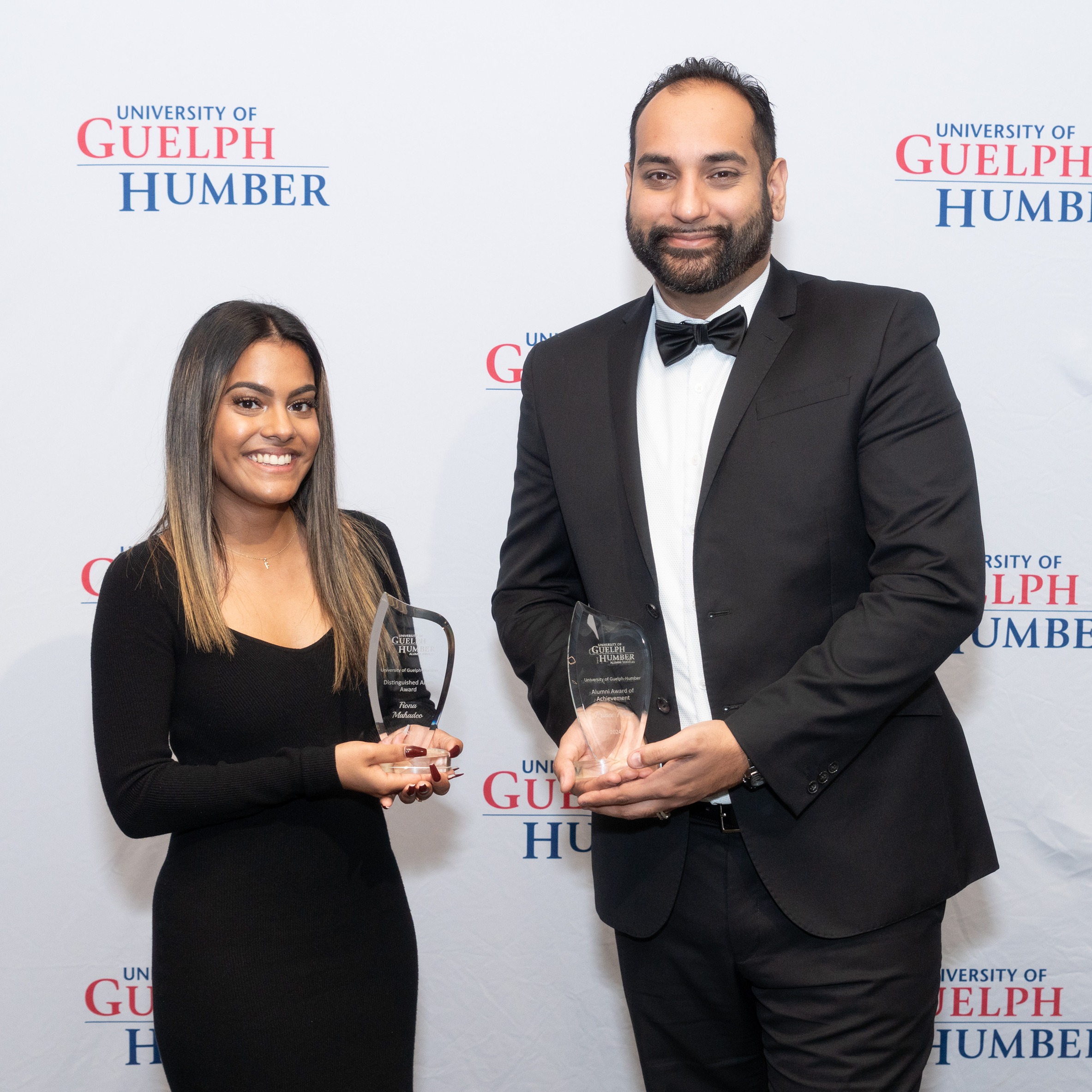 A woman and a man each hold a glass award