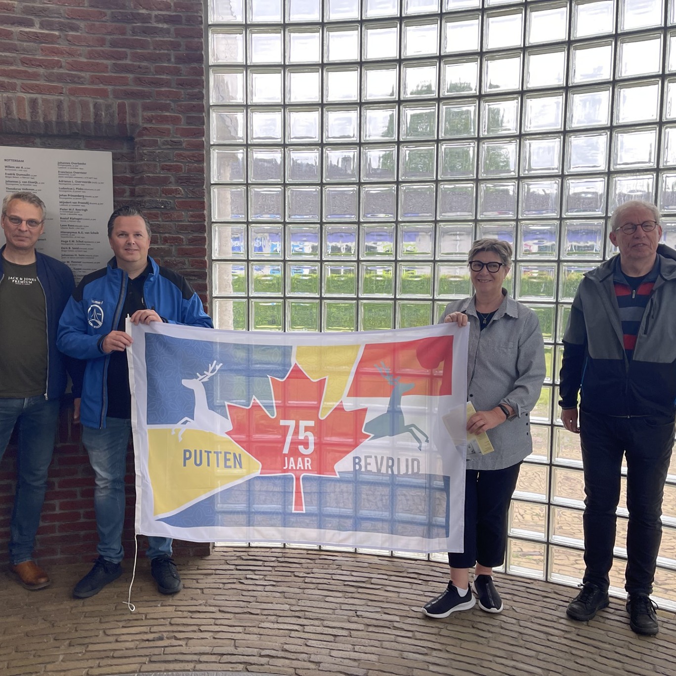 Four people holding commemorative flag by a window