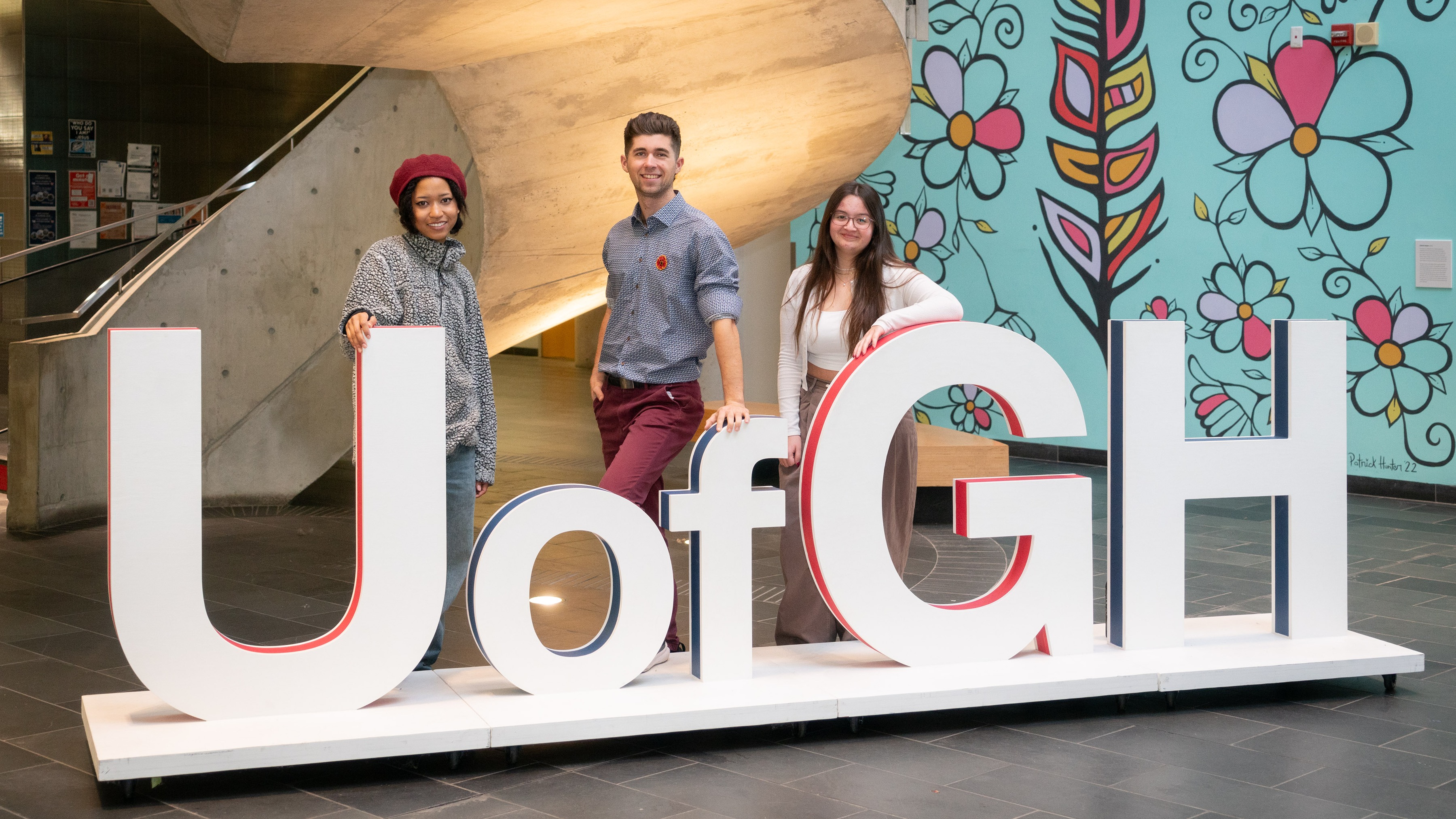 Three students pose in front of a large U of GH letter sign