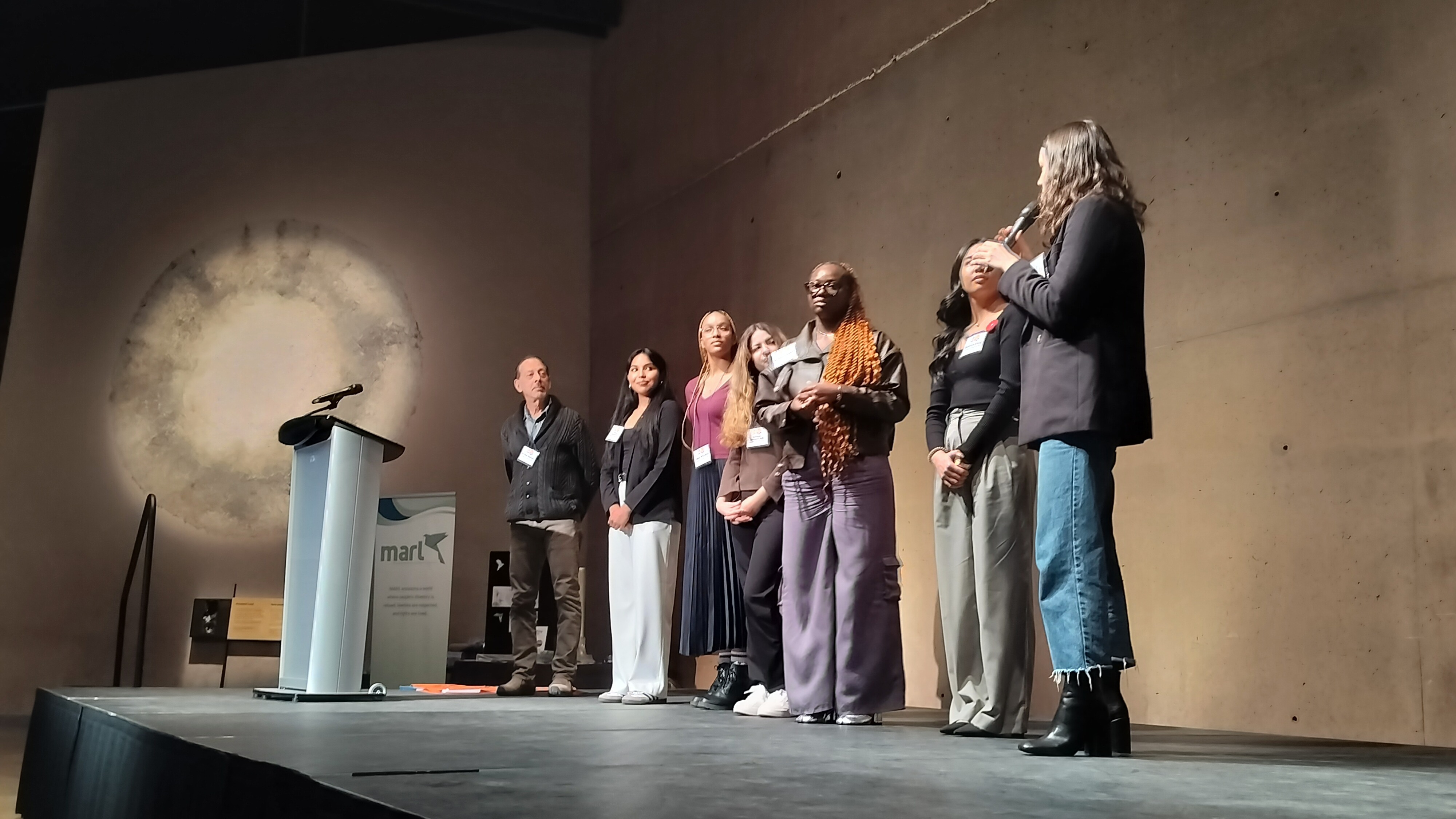 A group of seven people present on a stage