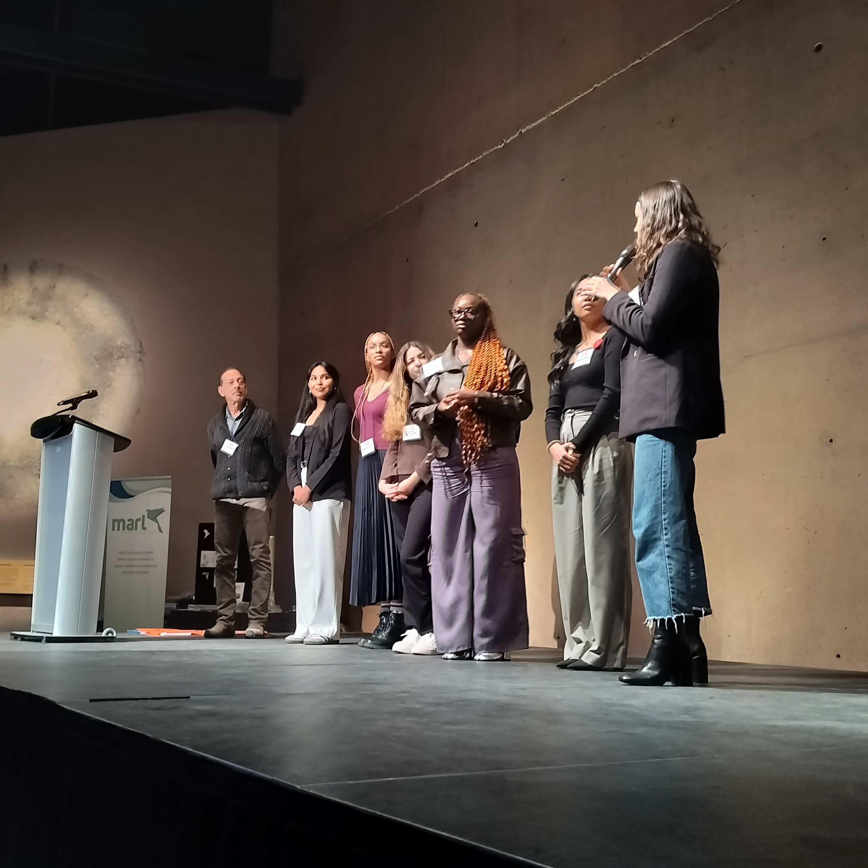 A group of seven people present on a stage