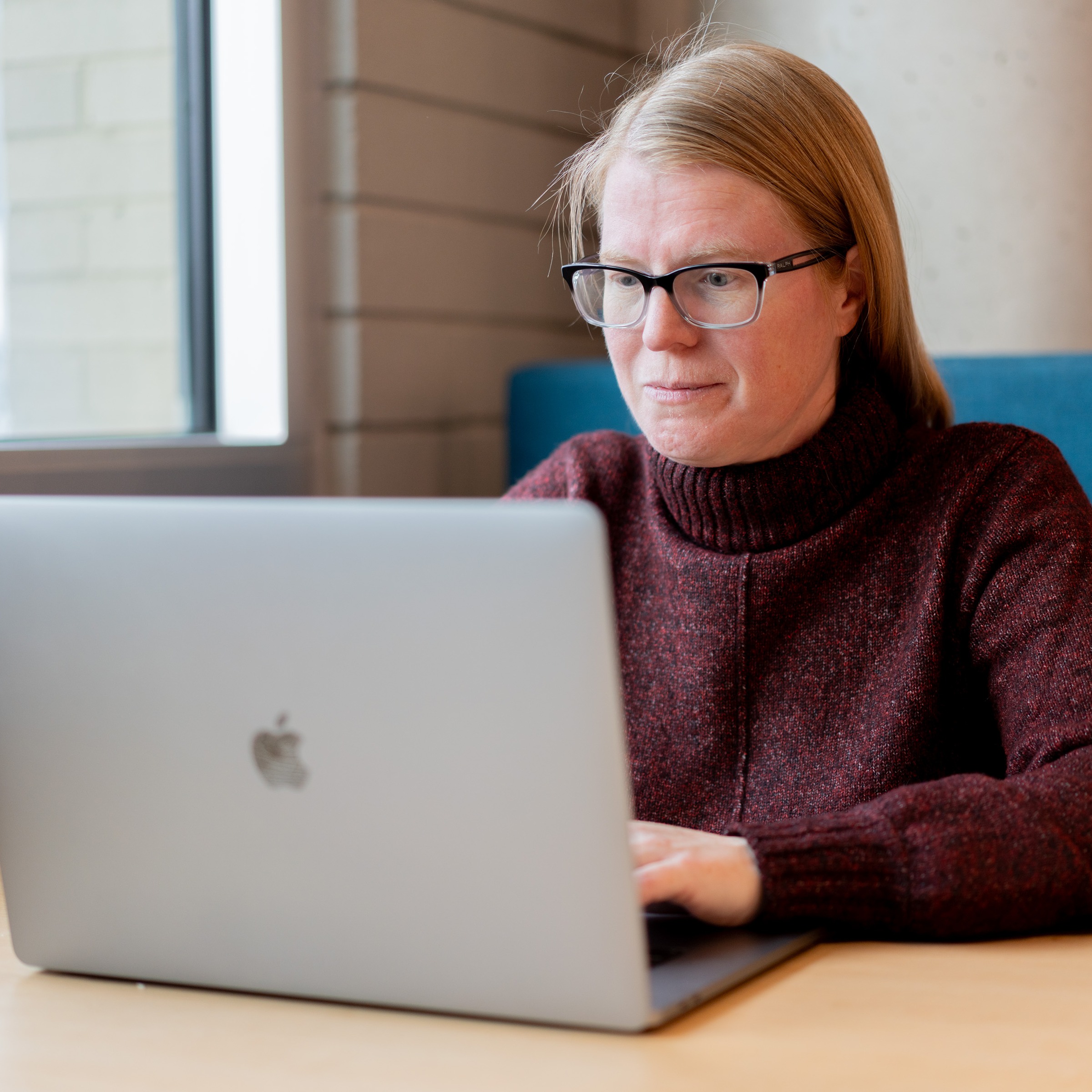 Laelie Snook sits on a blue couch and uses a laptop