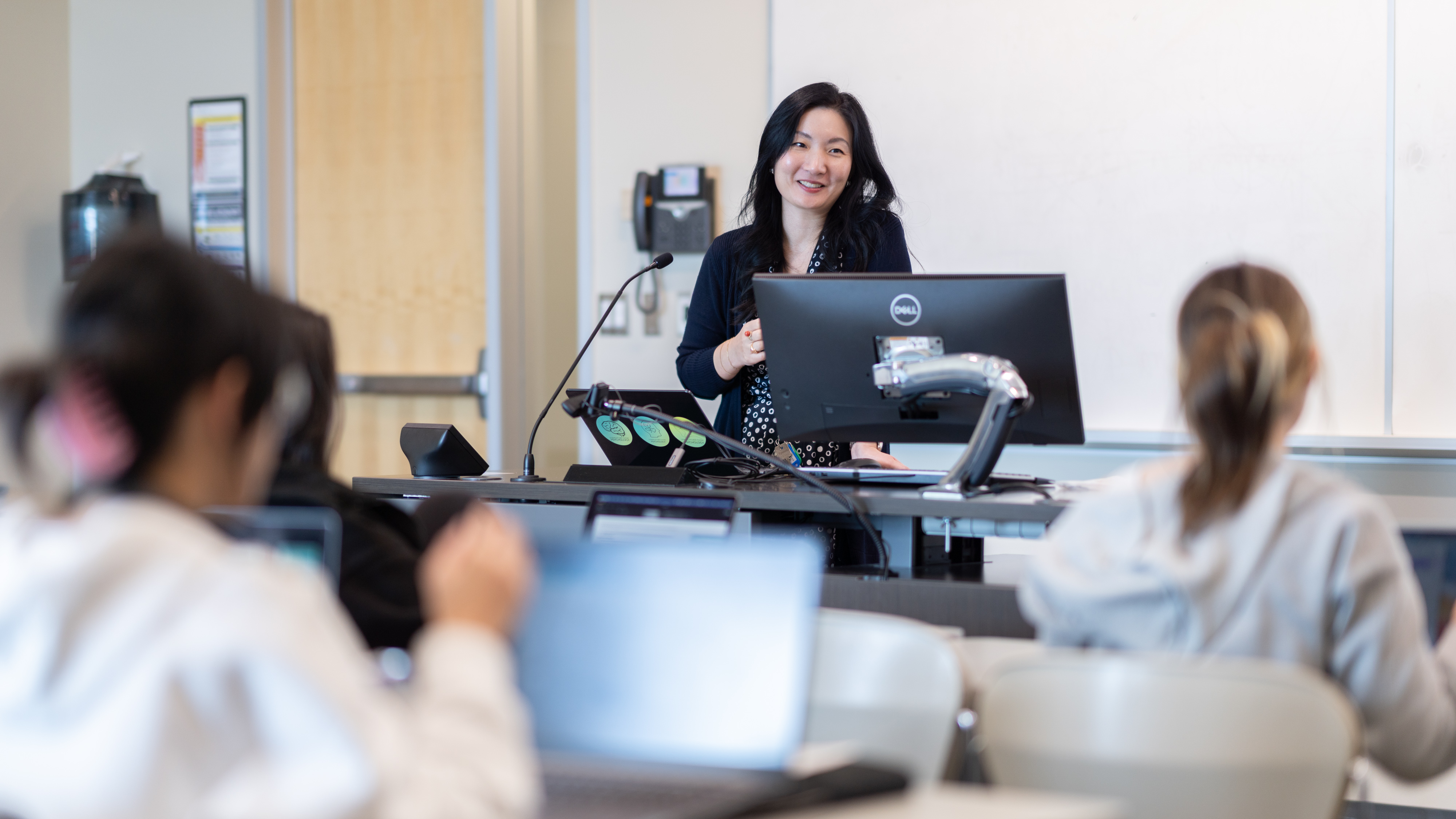 Alice Kim delivers a lecture behind a desk with a computer with a student audience in the foreground