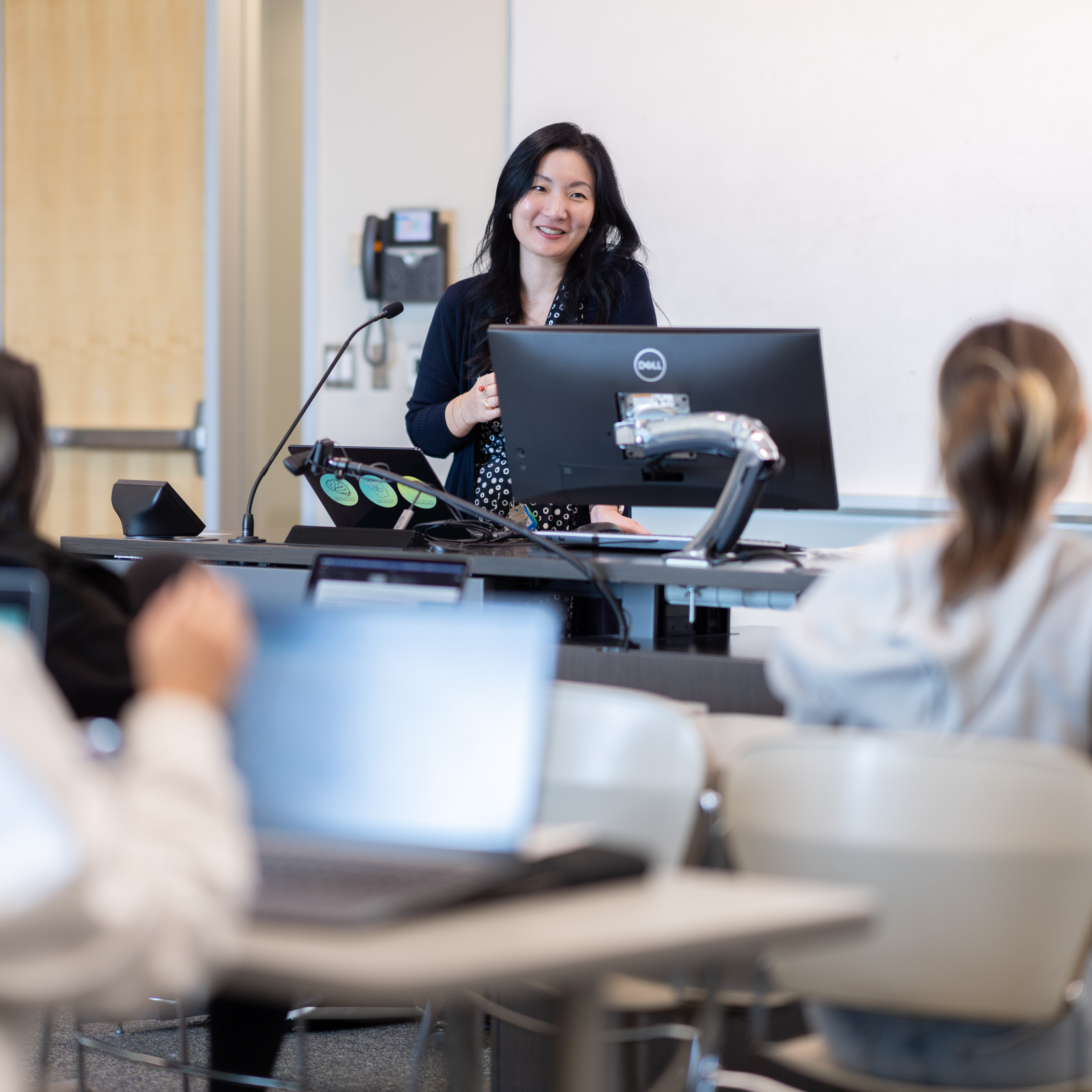 Alice Kim delivers a lecture behind a desk with a computer with a student audience in the foreground