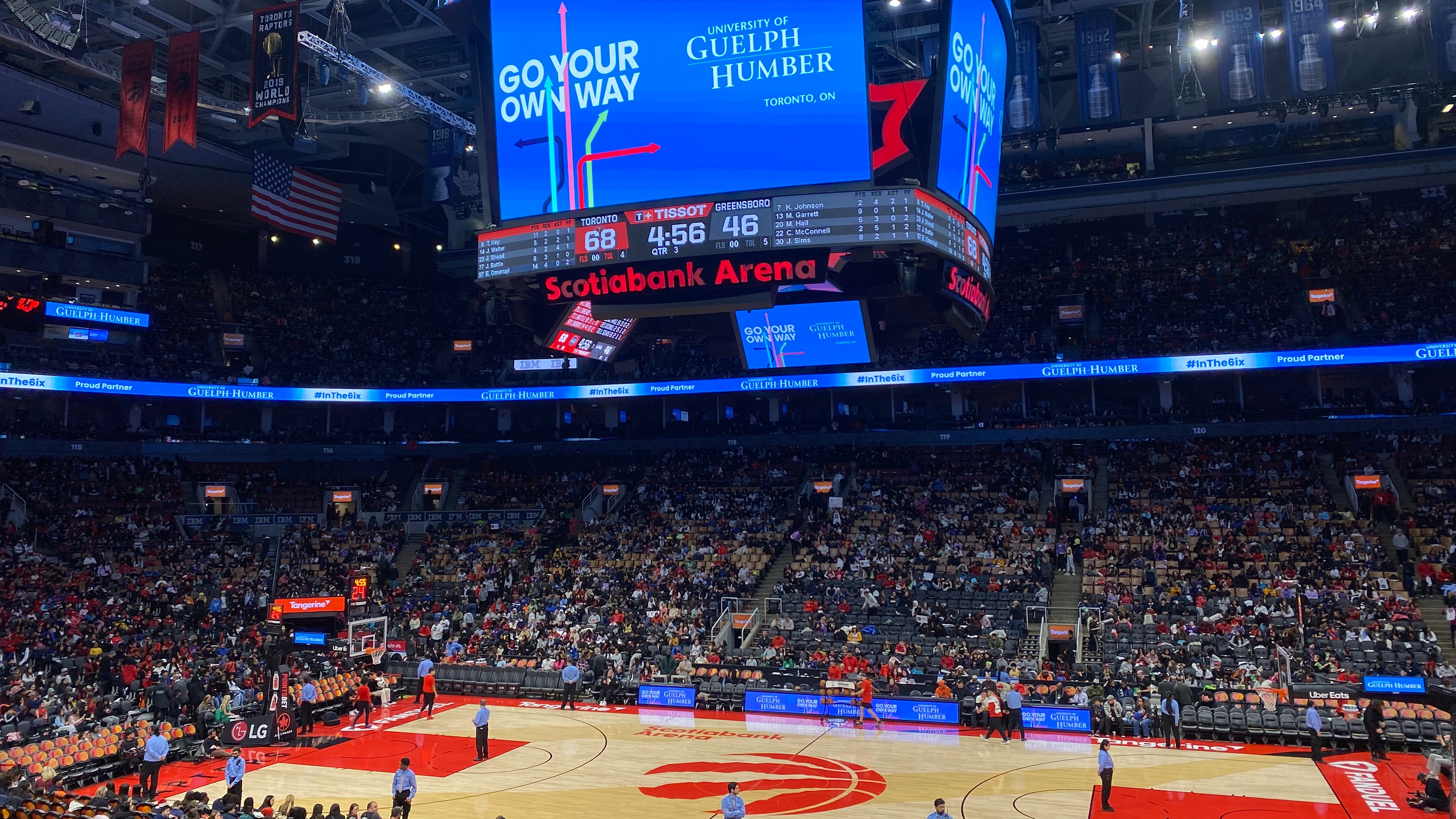 A basketball court inside the Scotiabank Arena is shown as seats are filling up with people, as a jumbotron hangs above the court with a University of Guelph-Humber advertisement