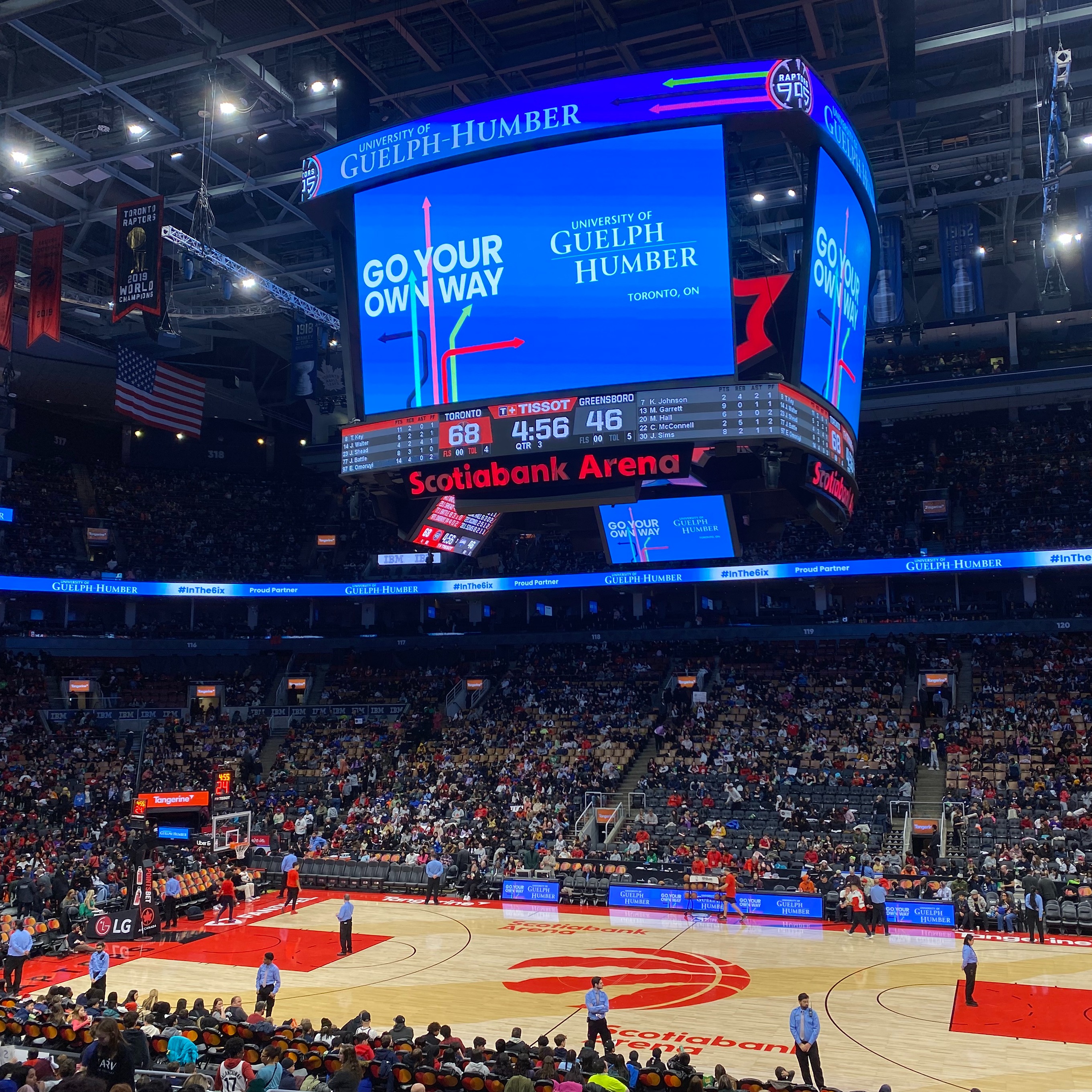 A basketball court inside the Scotiabank Arena is shown as seats are filling up with people, as a jumbotron hangs above the court with a University of Guelph-Humber advertisement