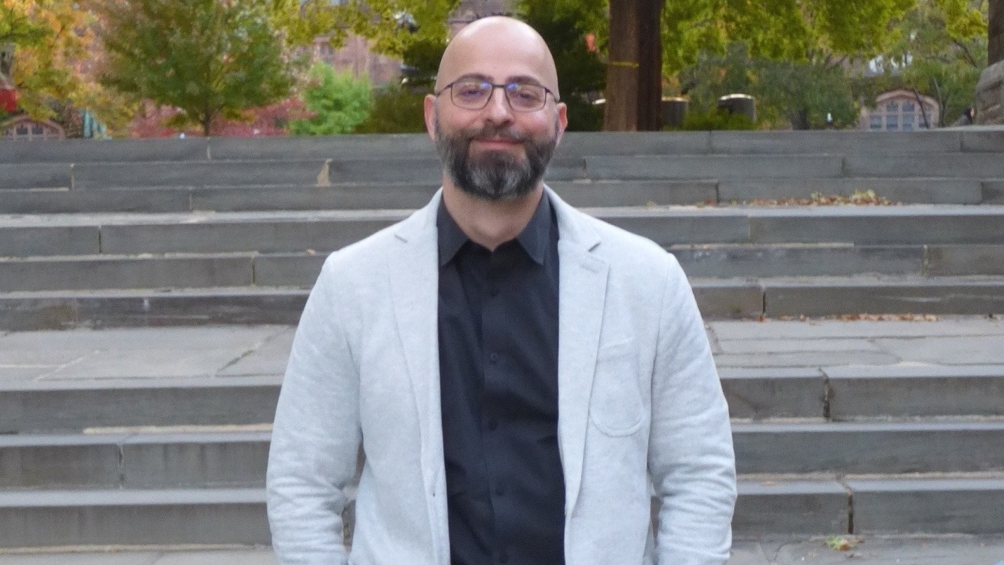 Dr. Molos poses in a grey blazer in front of stairs and trees