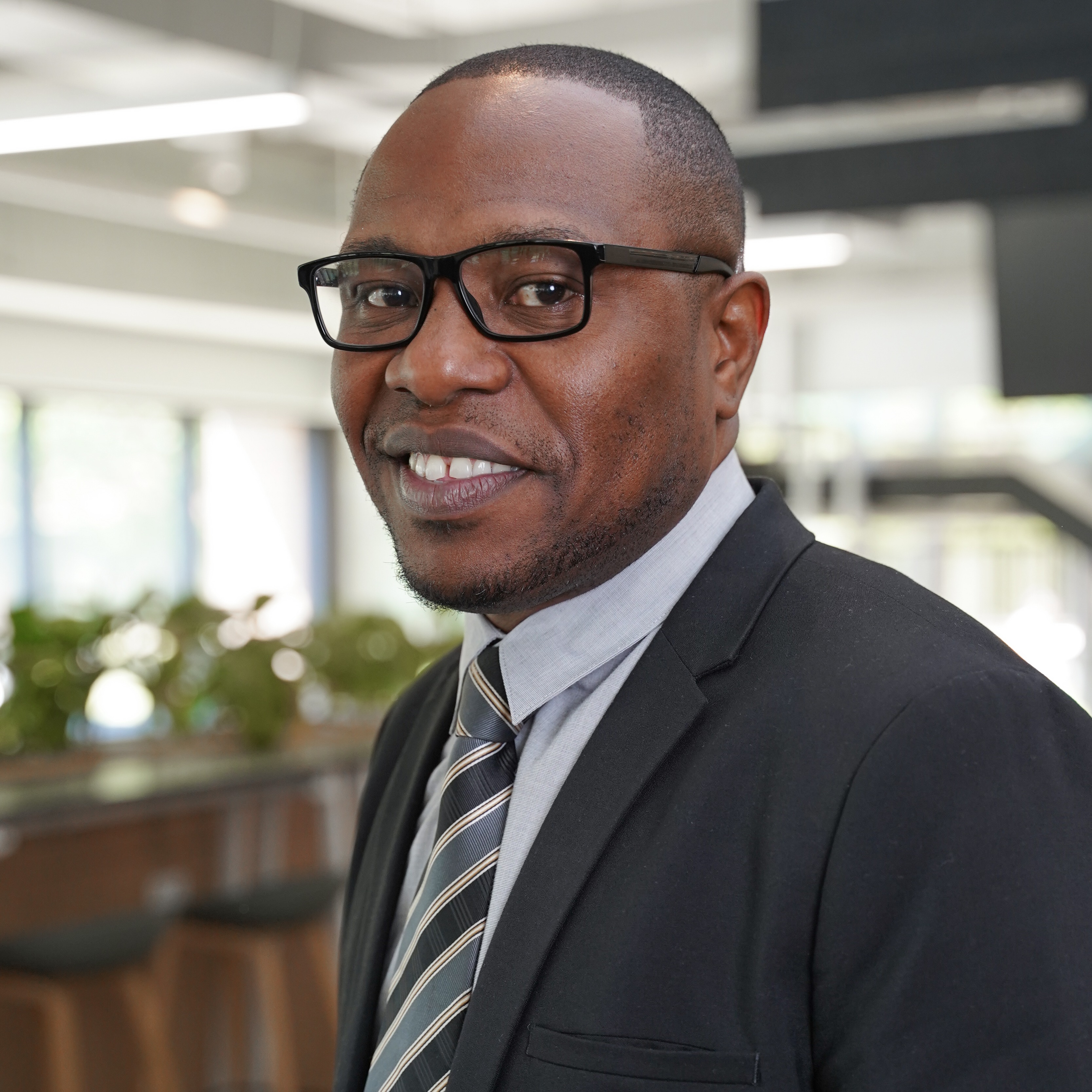 Karey Rowe wears glasses, a blazer, and tie as he looks into the camera smiling