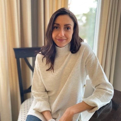 Olivia Boukydis poses for a photo sitting on a chair wearing a turtleneck sweater